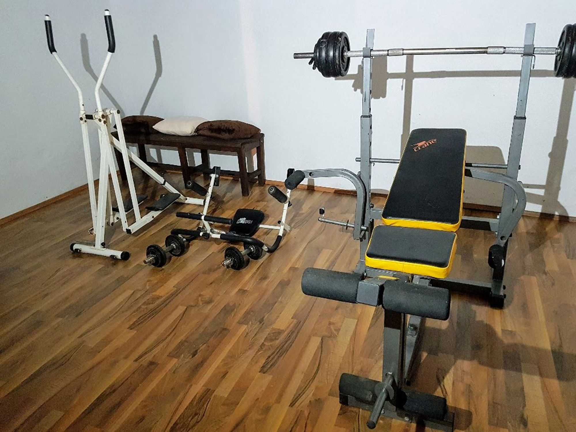 Fitneszterem súlyzópaddal, cross trainerrel és súlyzókkal a fapadlón.
