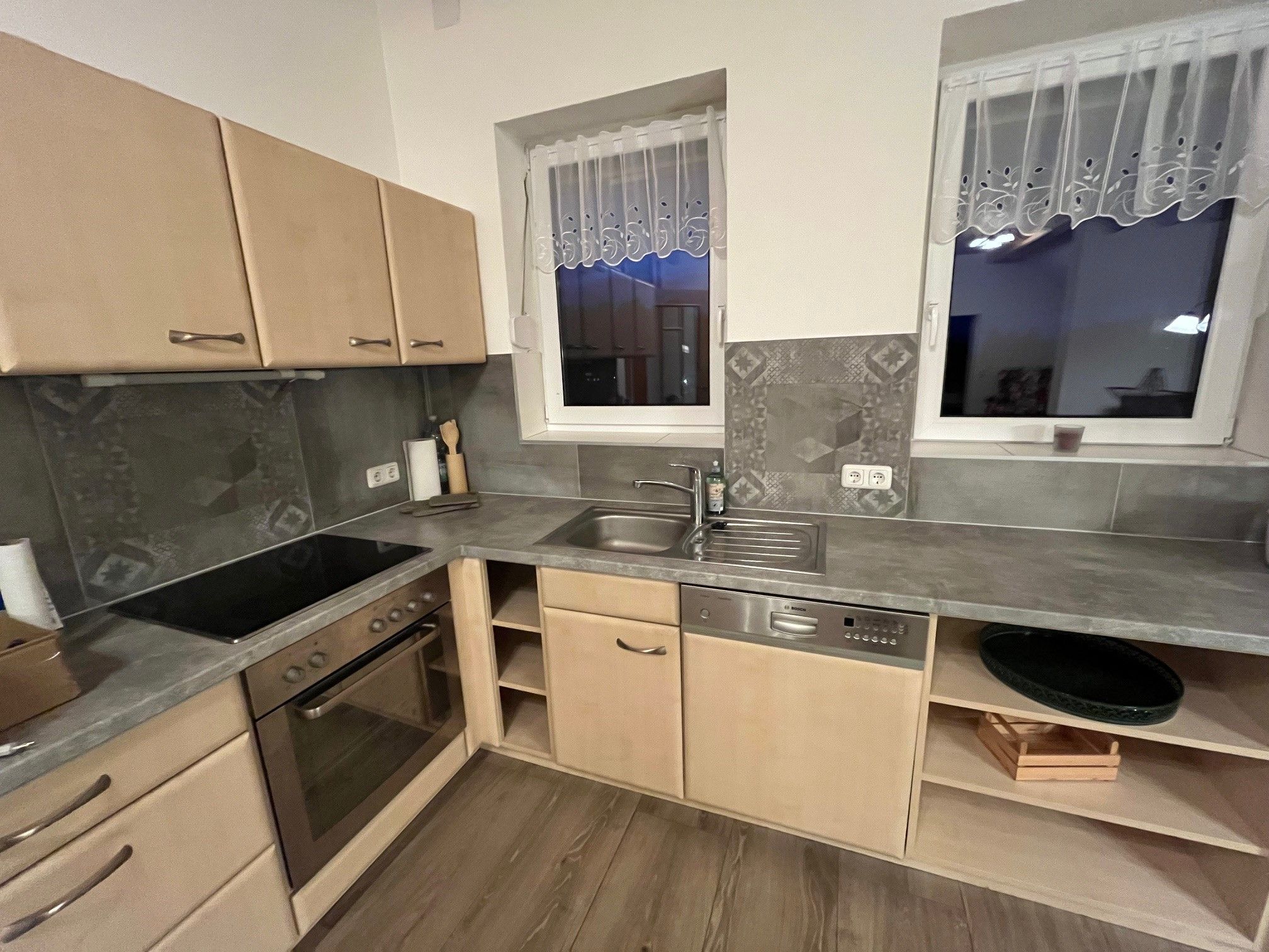 Modern konyha fa szekrényekkel, elektromos tűzhely, mosogató és mosogatógép.