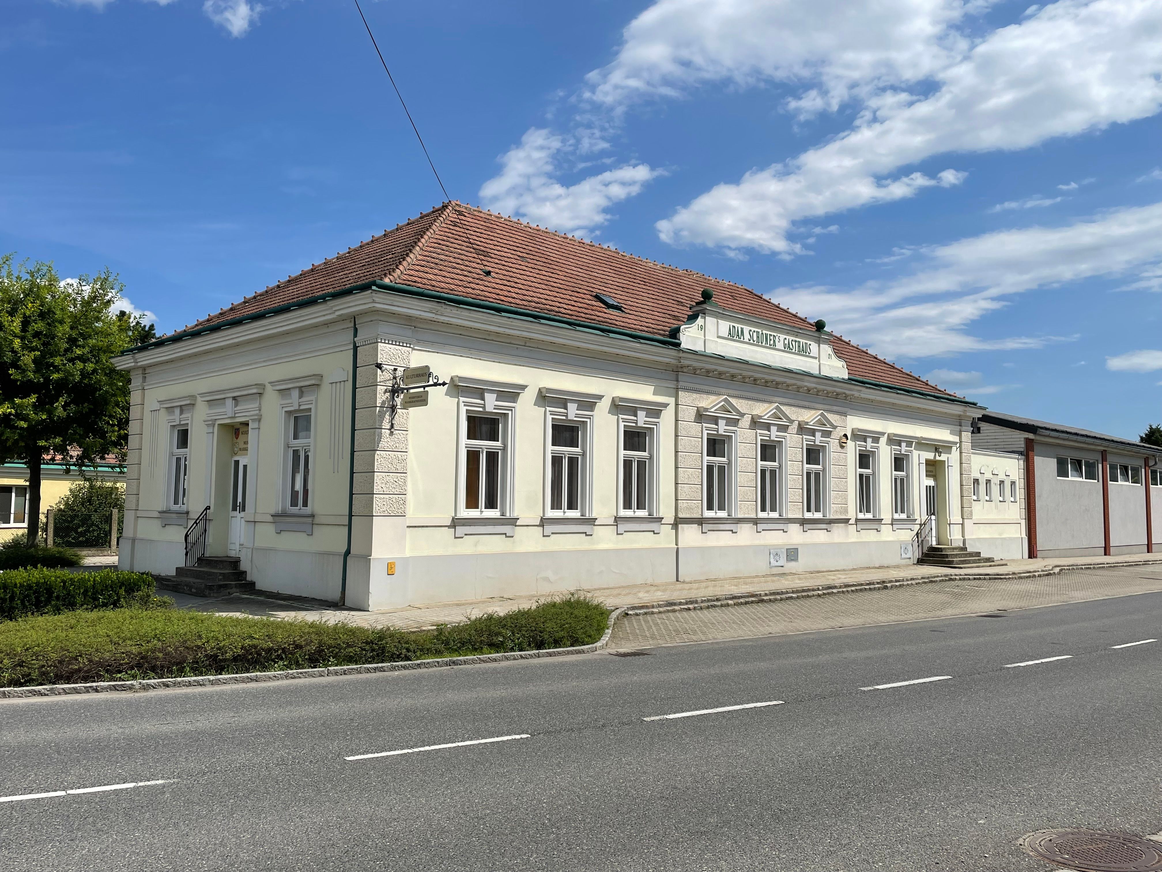 A Kulturhaus, egy világos, történelmi épület vörös cseréptetővel, egy utca mellett áll a kék ég alatt.