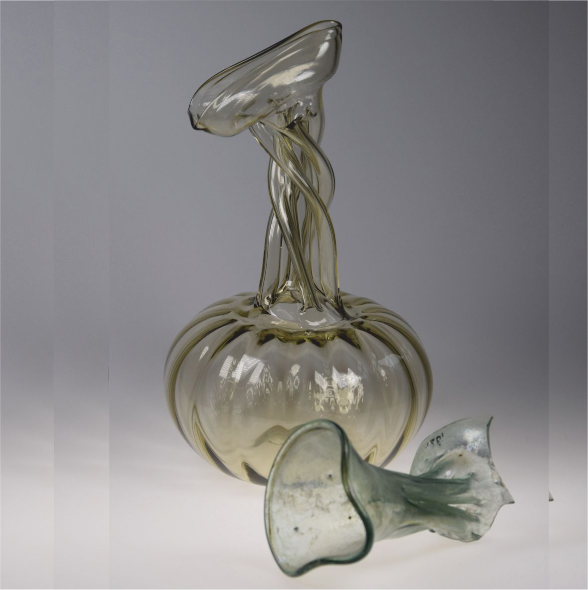 Csavart formájú üvegtárgy szürke háttéren.