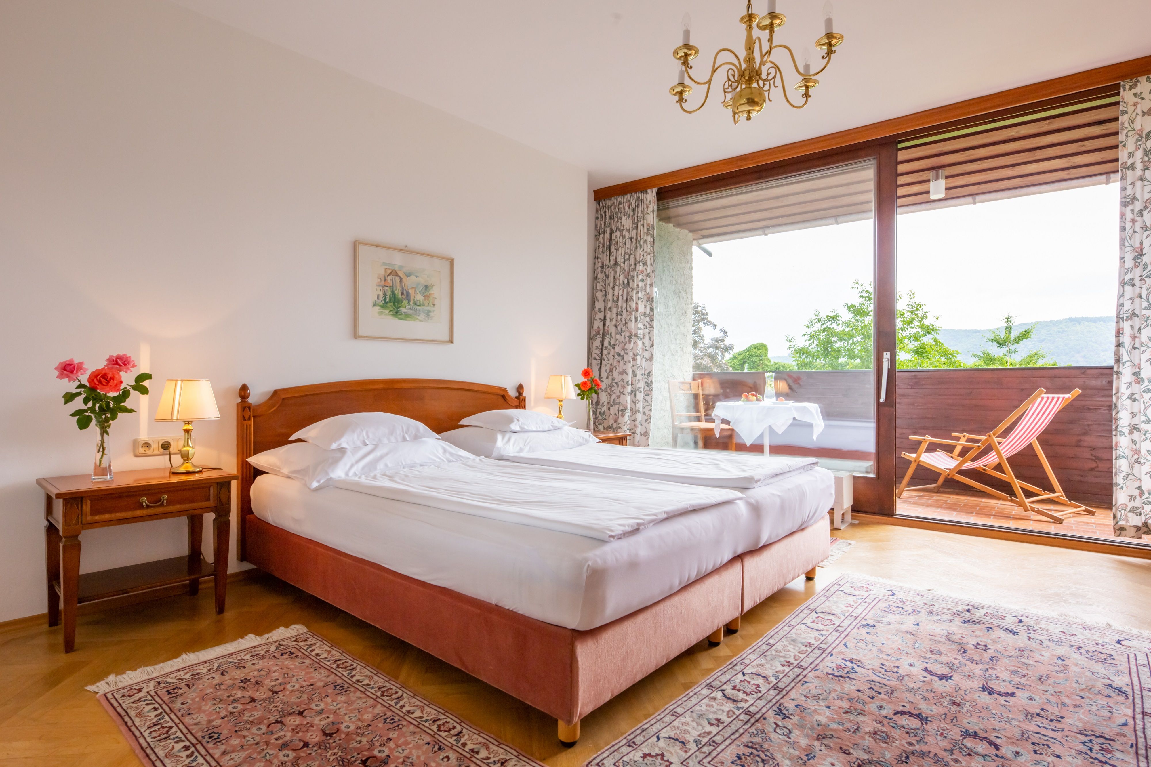 Hangulatos hálószoba franciaággyal, éjjeli lámpákkal és erkéllyel, napozószékkel és asztallal.