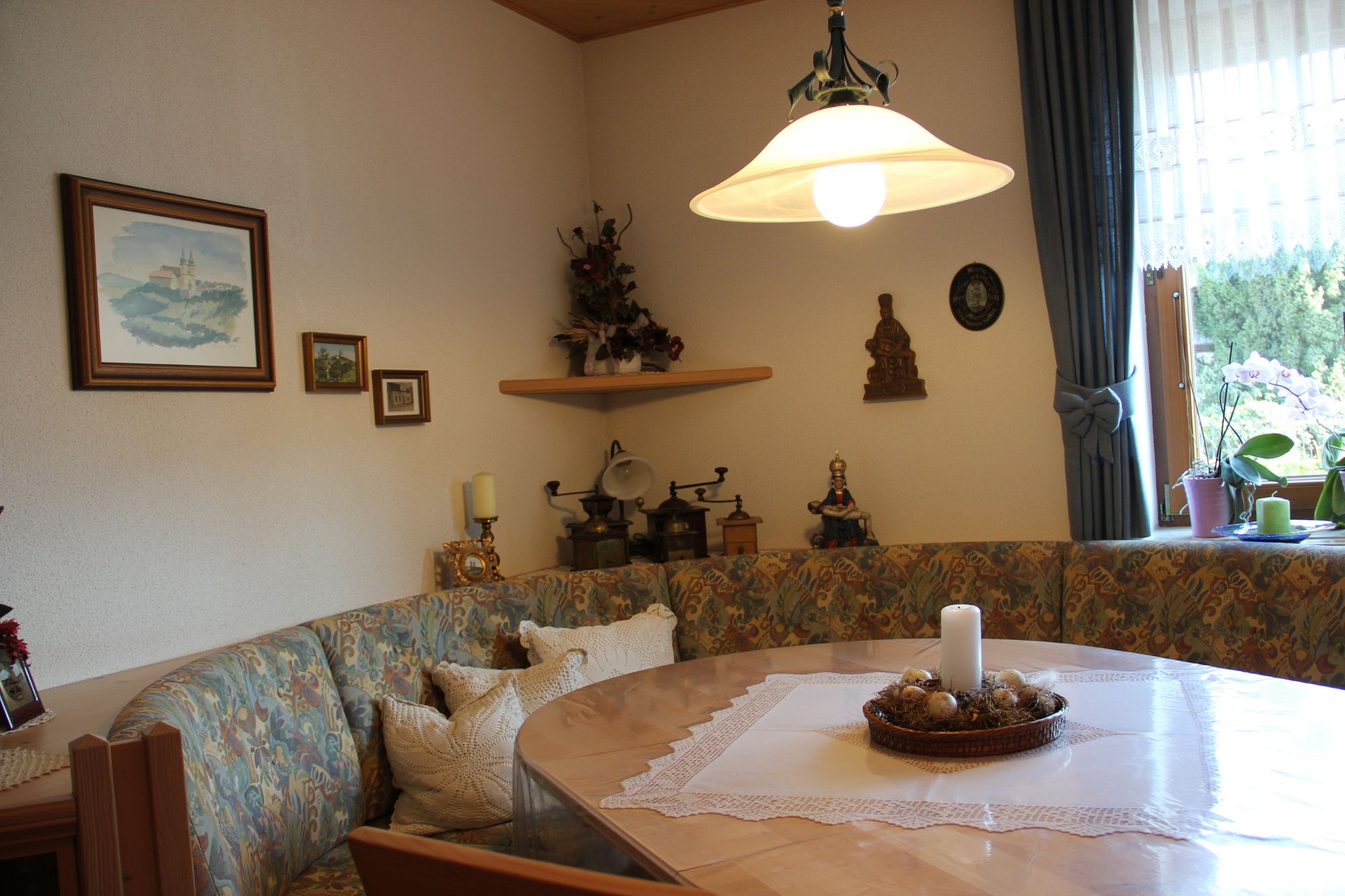 Hangulatos reggelizőszoba sarokpaddal, asztallal, gyertyával és dekorációval a falon.