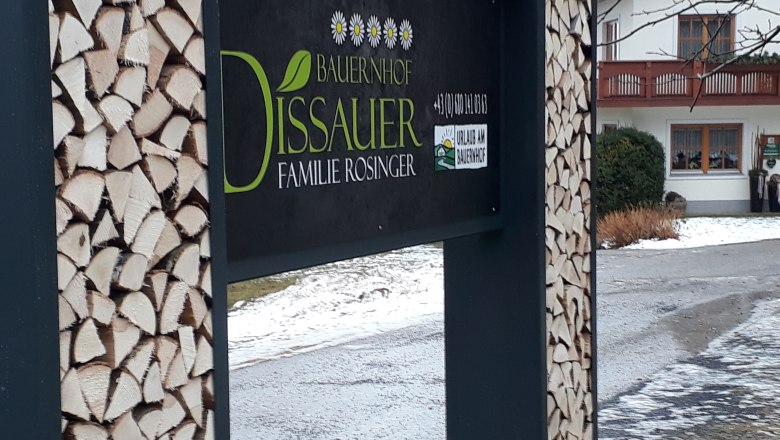 Egy farm jele, a háttérben fakupacokkal és egy házzal.