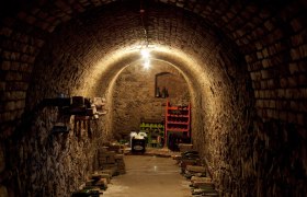 Egy keskeny, bolt&iacute;ves borospince t&eacute;glafalakkal &eacute;s t&aacute;rolt palackokkal.