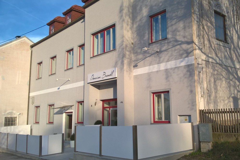 A Brandl panzió külső nézete szürke homlokzattal és piros ablakkeretekkel.