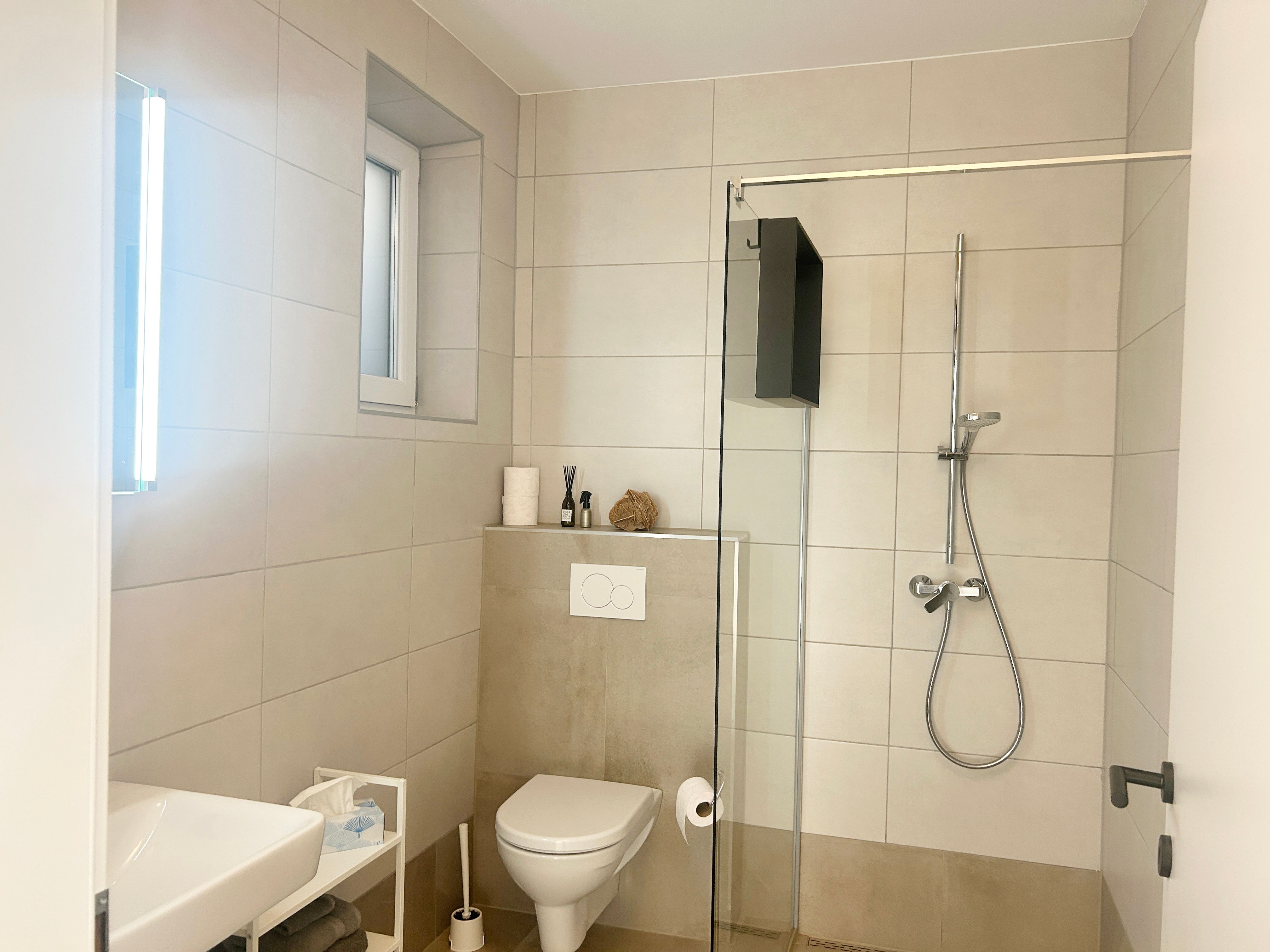 Modern fürdőszoba zuhanyzóval, WC-vel és mosdókagylóval.