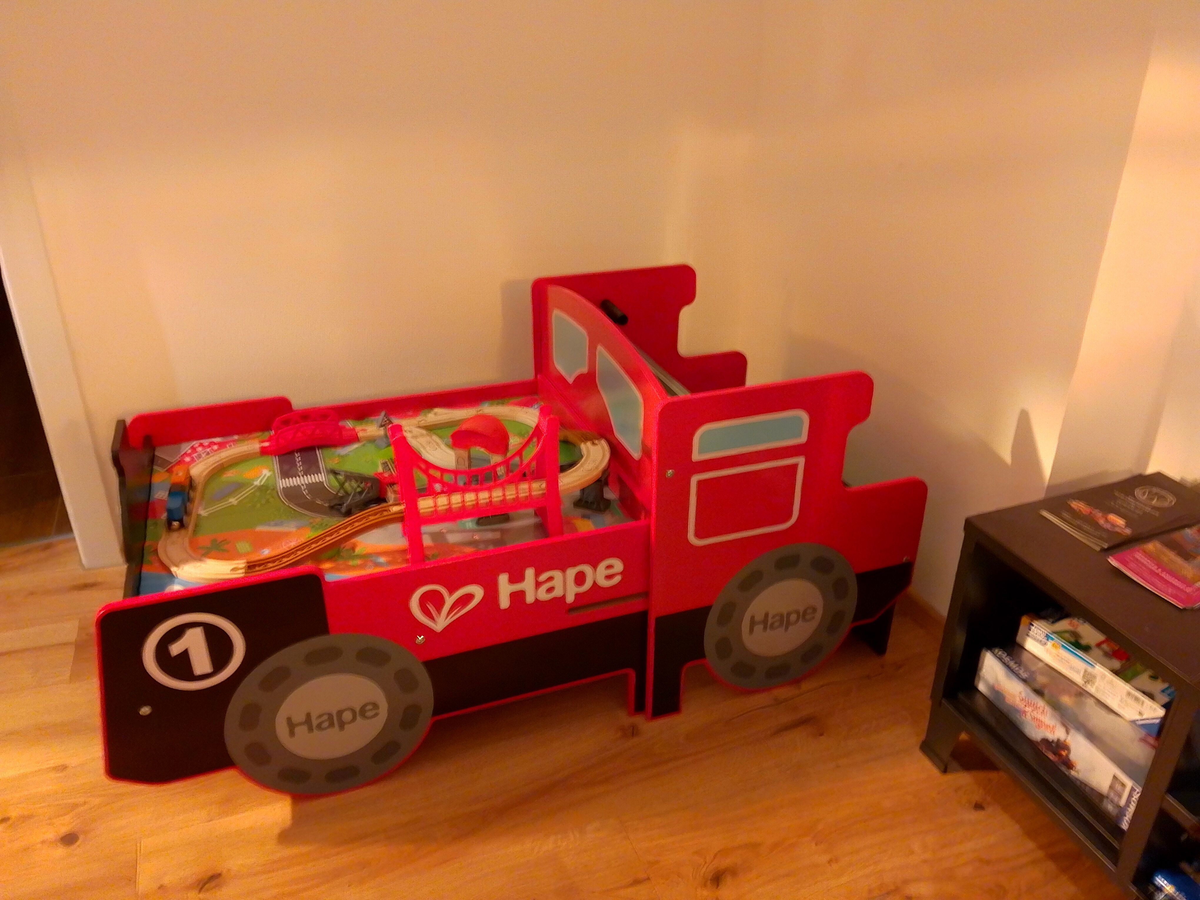 Piros játékágy mozdony alakú játékvasúttal.