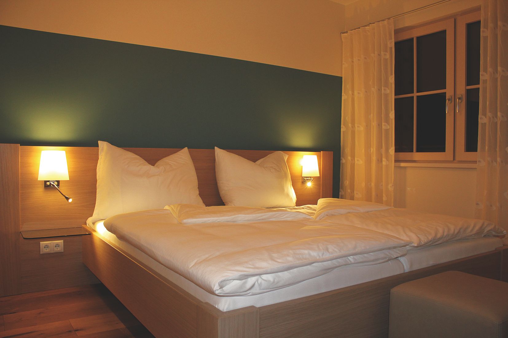 Hangulatos vendégszoba franciaággyal, két éjjeli lámpával és függönyös ablakkal.