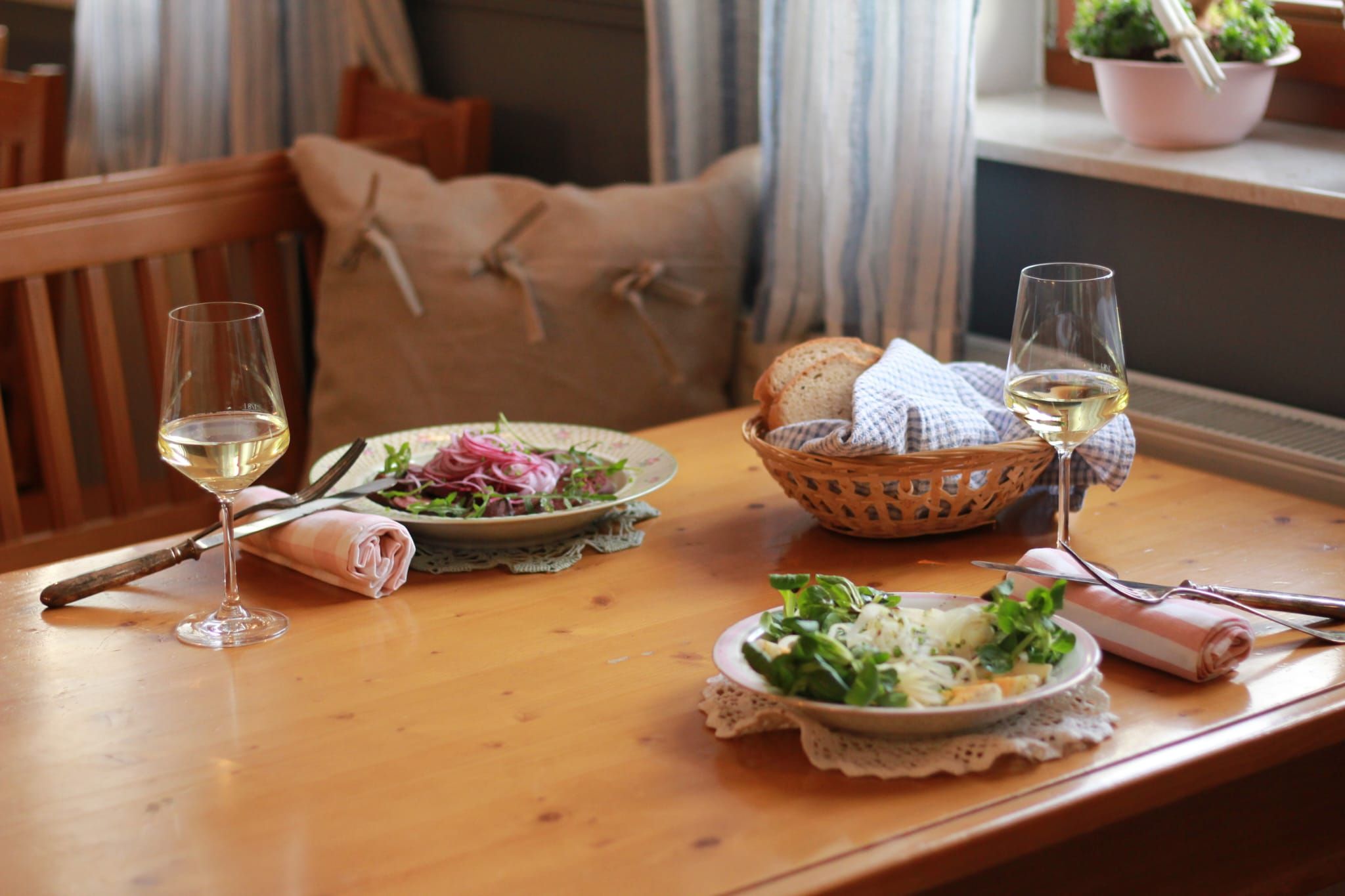 Két tányér saláta és két pohár fehérbor egy faasztalon, mellette egy kenyérkosár.