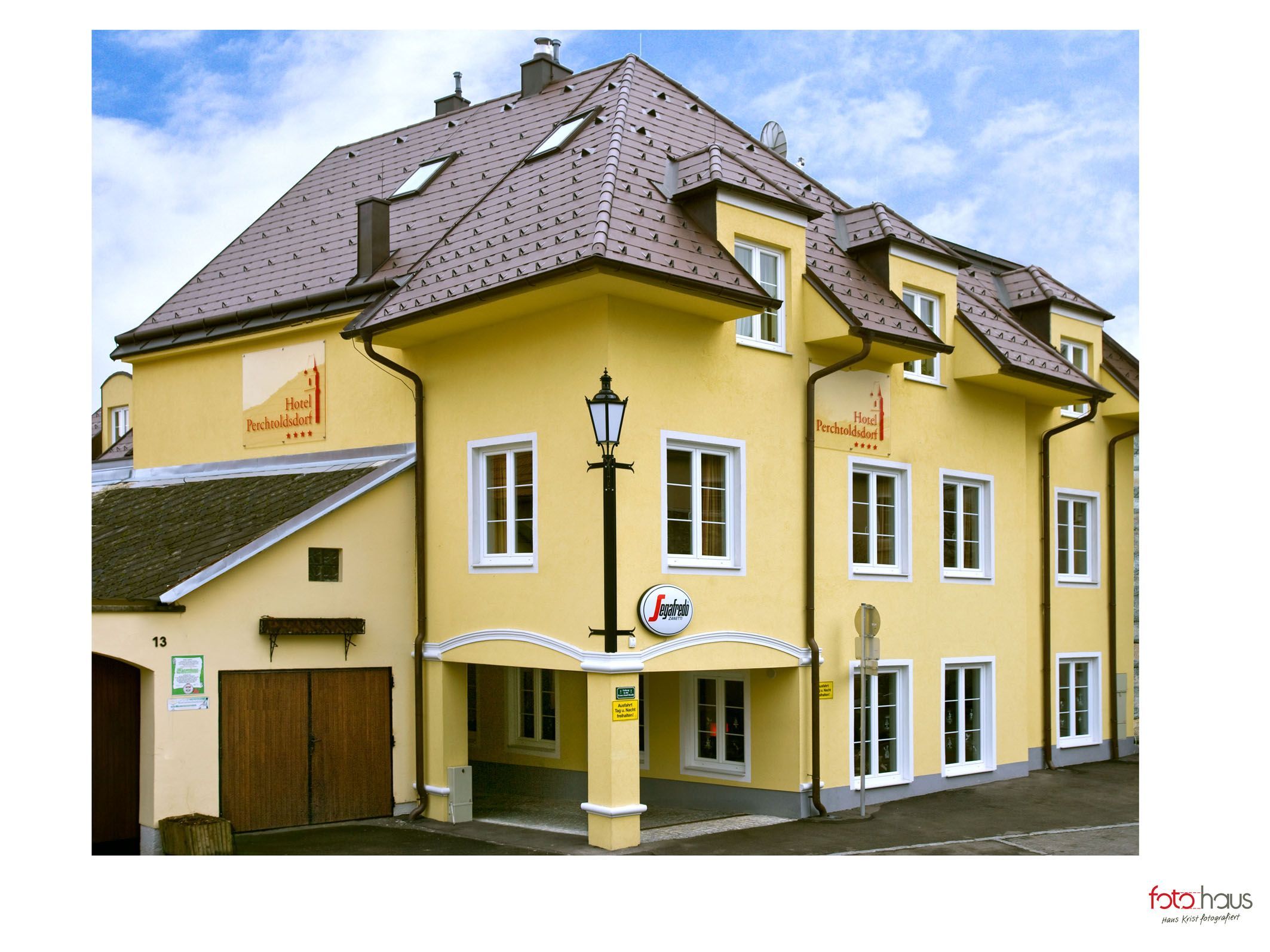 Sárga szállodaépület több ablakkal és egy táblával, amelyen a "Hotel Perchtoldsdorf" felirat olvasható.