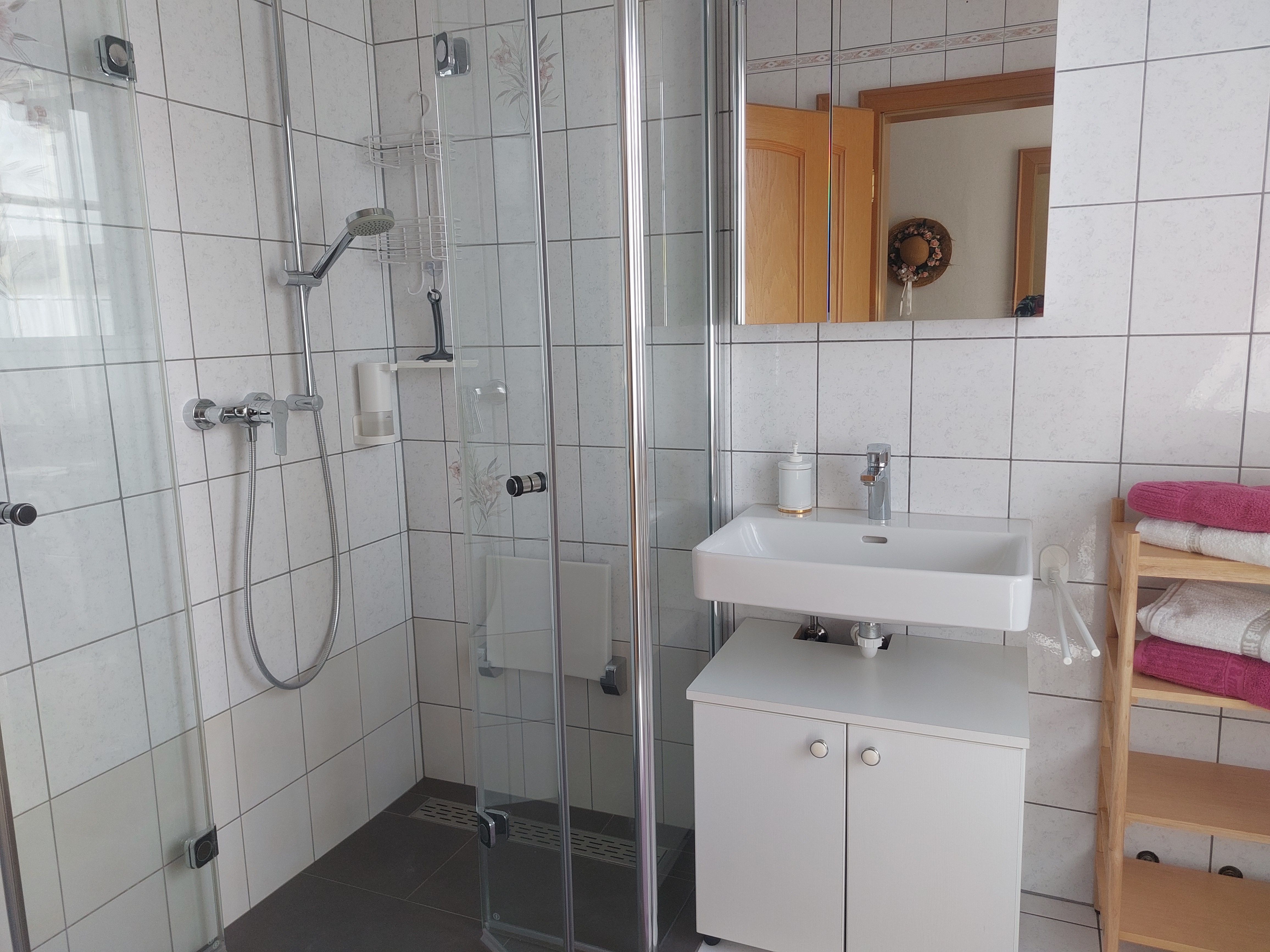Modern fürdőszoba zuhanyzóval, mosdóval és törölközőtartóval.