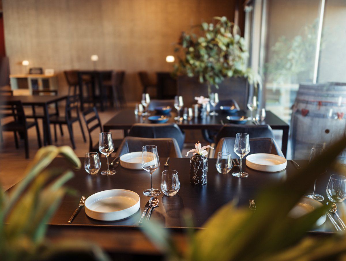 Elegáns étterem terített asztalokkal, borospoharakkal és növényekkel a háttérben.