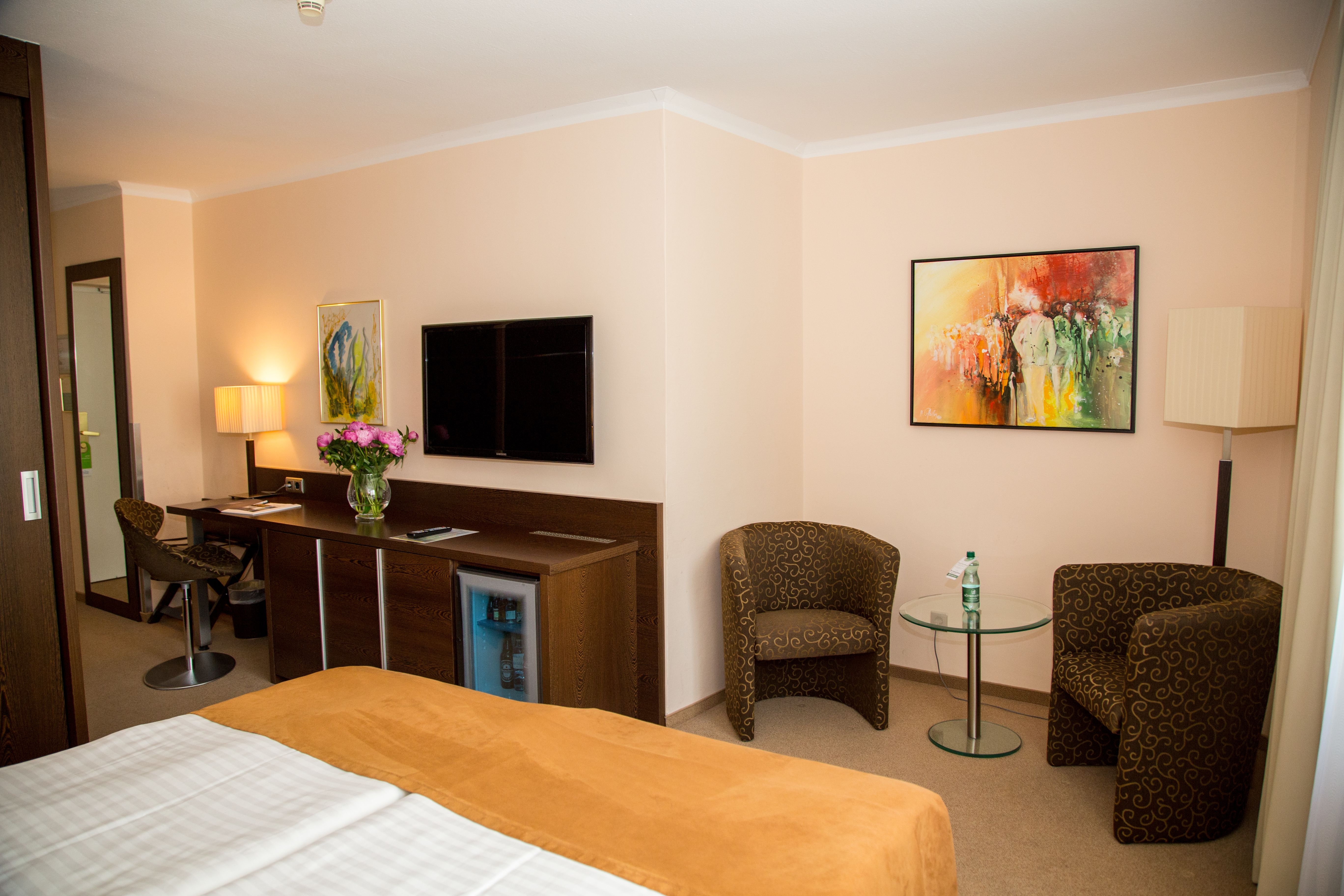 Hotelszoba franciaággyal, íróasztallal, televízióval és két karosszékkel.