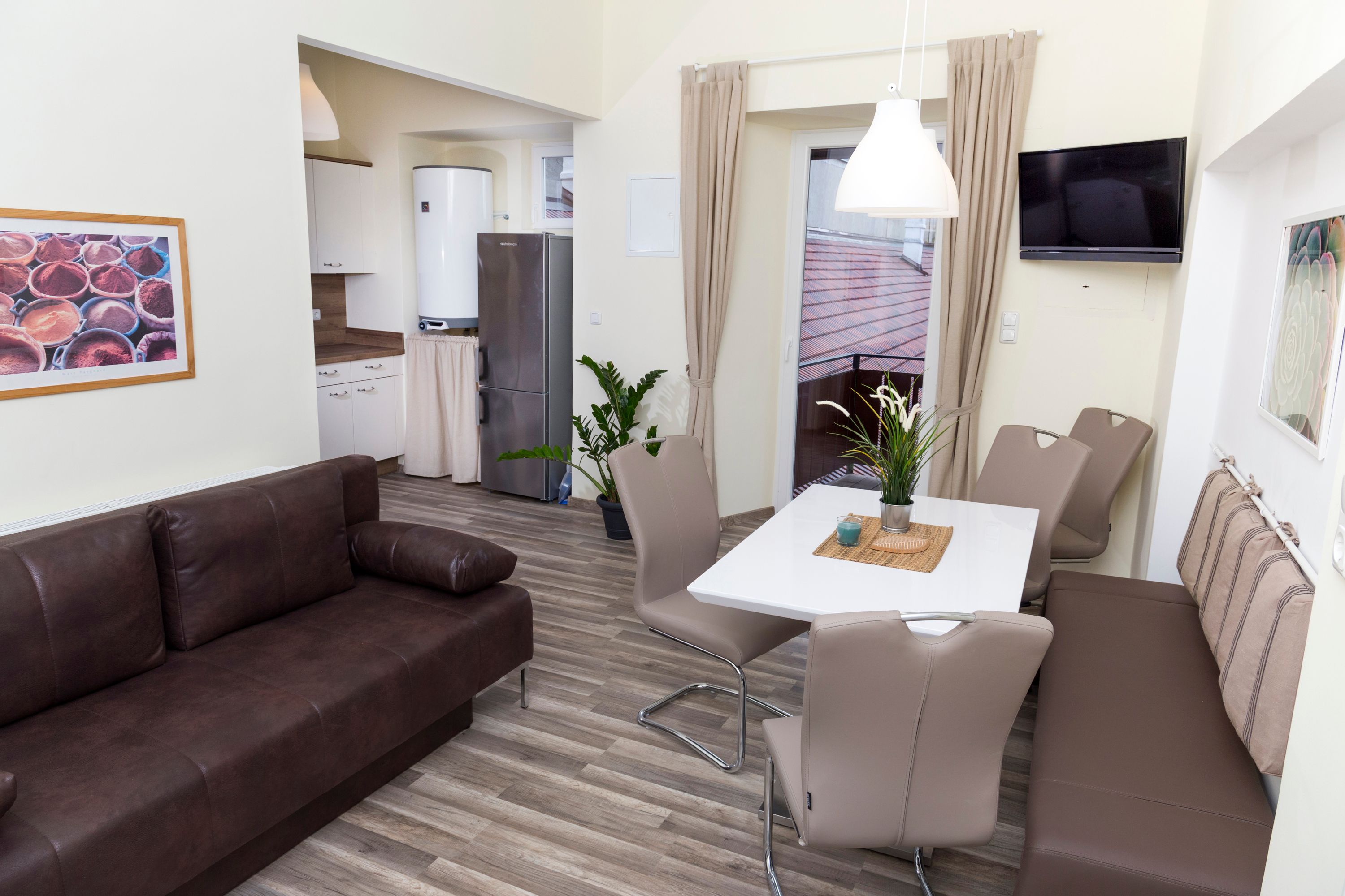 Modern konyha barna kanapéval, étkezőasztallal és székekkel, hűtőszekrénnyel és növényekkel.