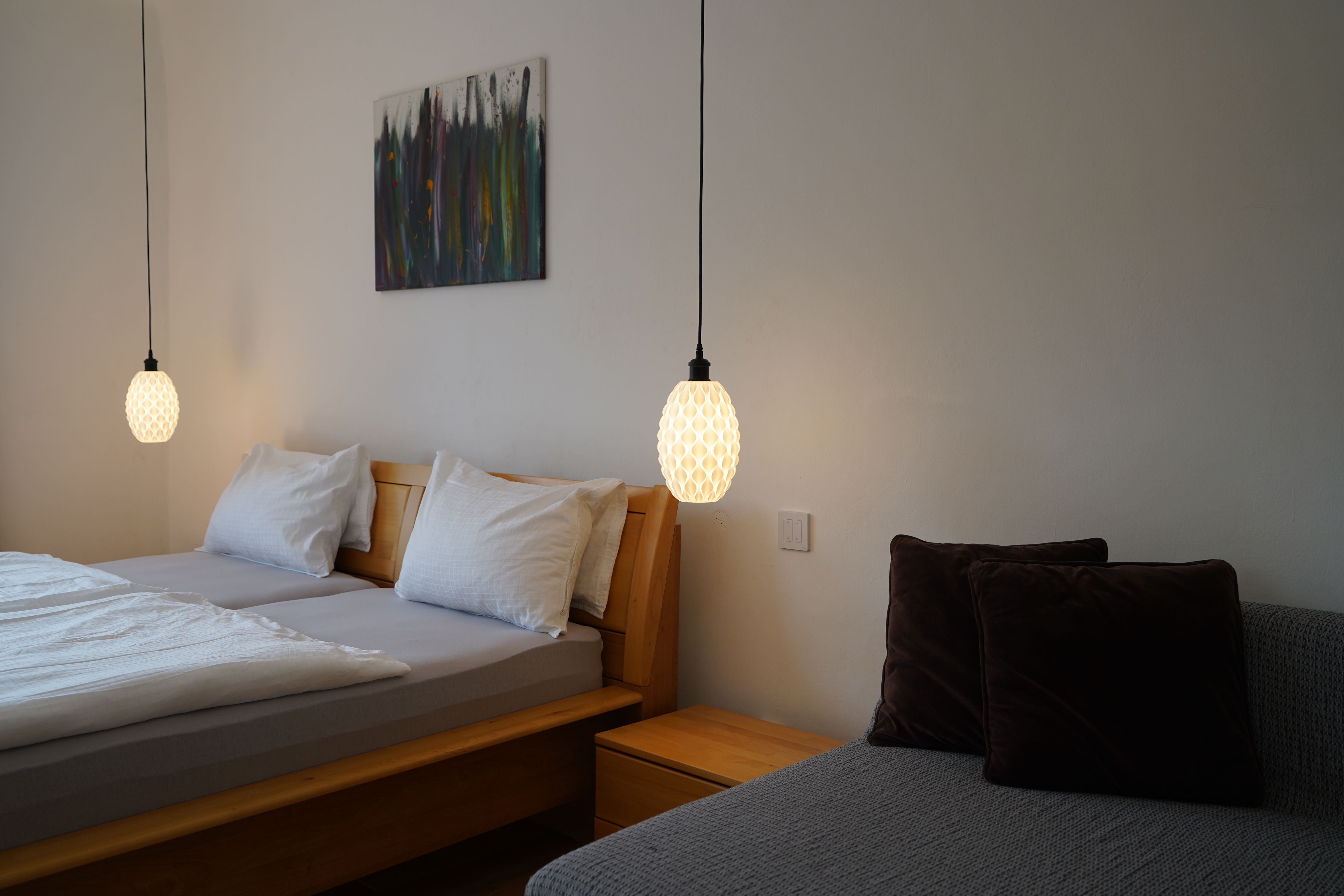 Hálószoba franciaággyal, két függőlámpával és egy párnás kanapéval.