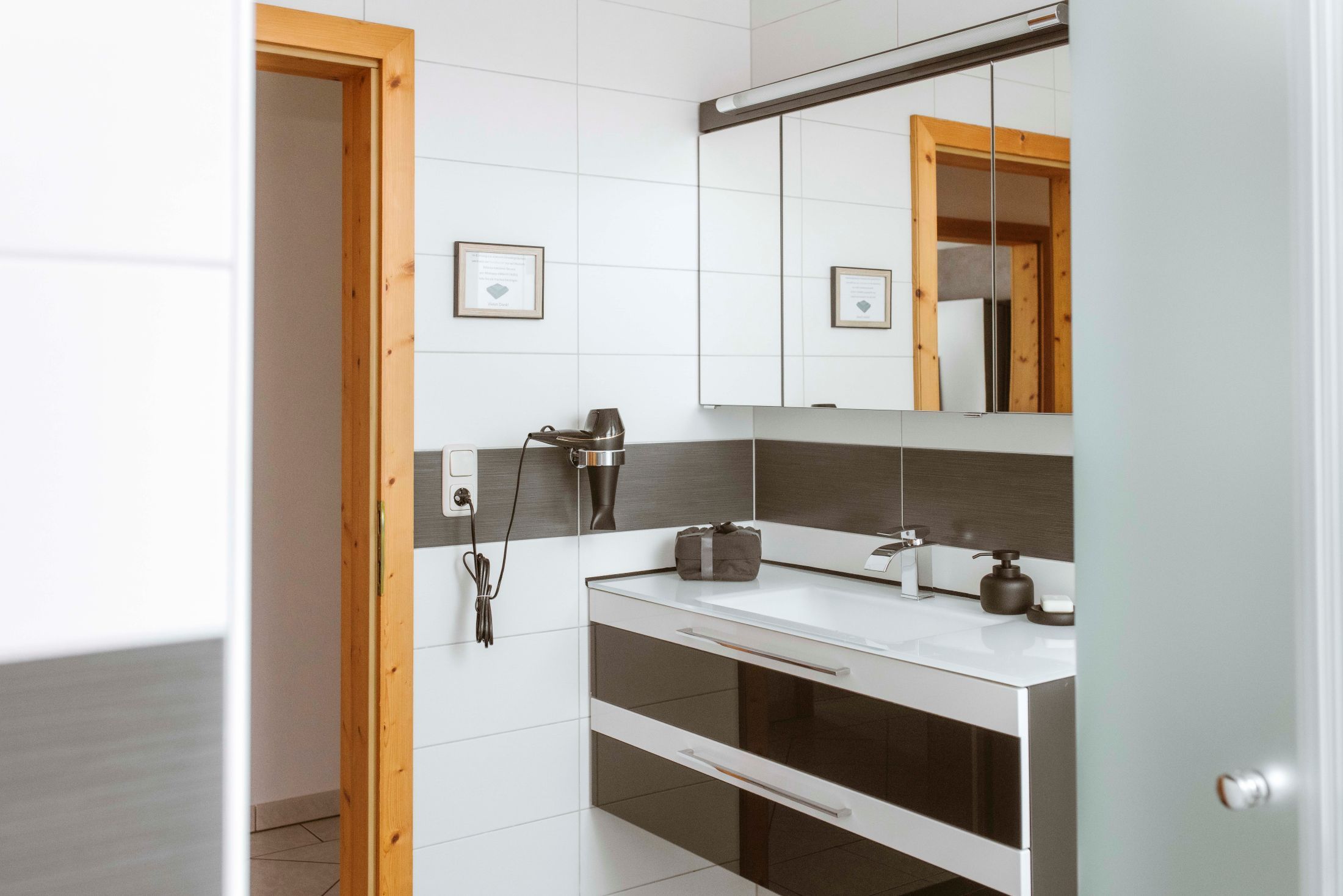 Modern fürdőszoba tükörrel, mosdókagylóval és hajszárítóval a falon.