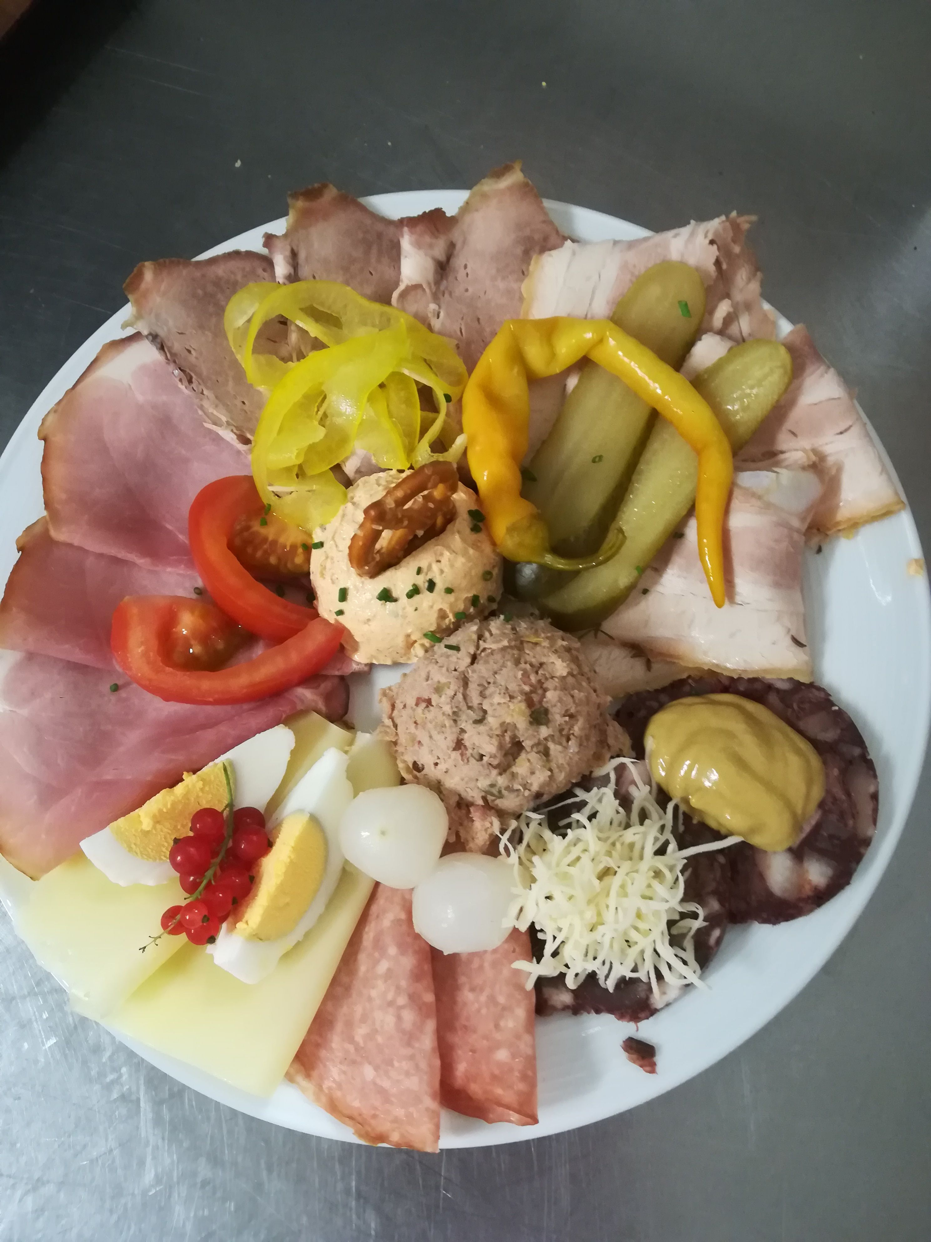 Egy tányér különböző kolbász- és sajtféleségekkel, tojással, hagymával, paprikával és kenőanyagokkal.