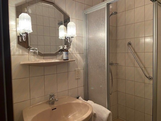Fürdőszoba mosdóval, tükörrel, zuhanyzóval és törölközővel.
