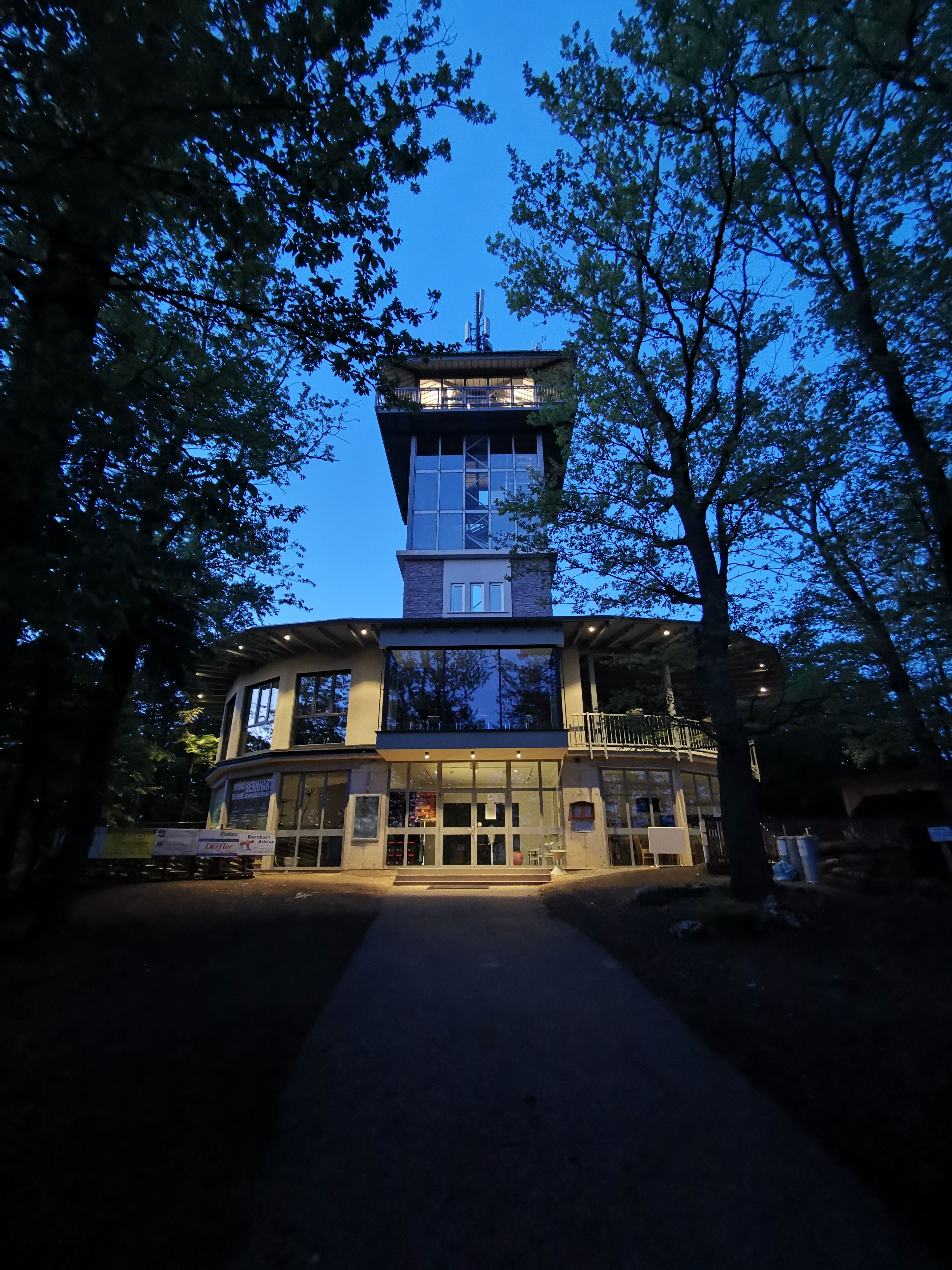 Ovális épület üveg kilátótoronnyal éjszaka.