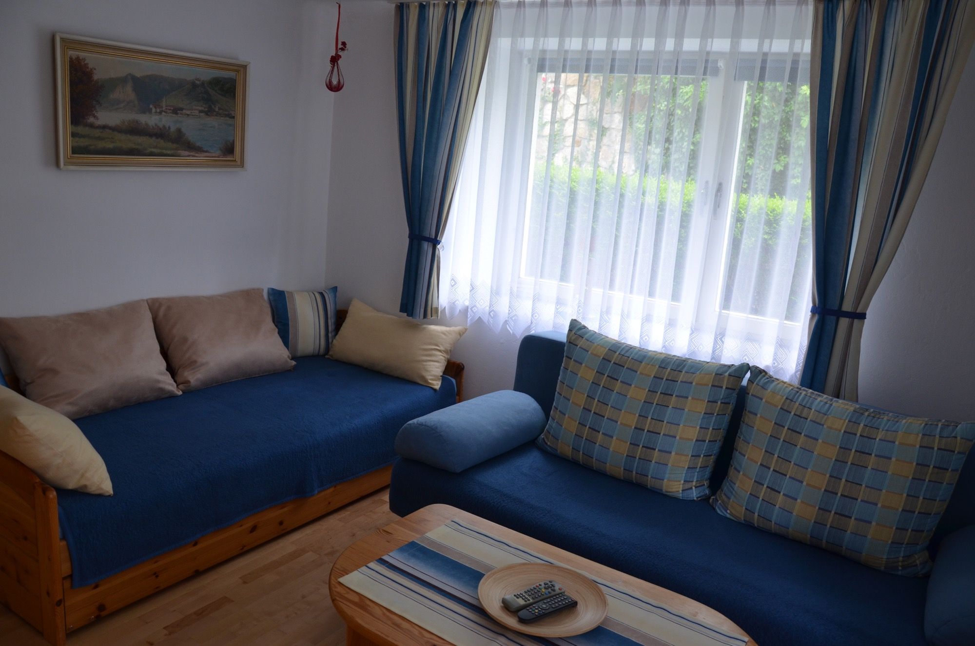 Hangulatos nappali kék kanapékkal, párnákkal, fa asztallal és függönyös ablakkal.