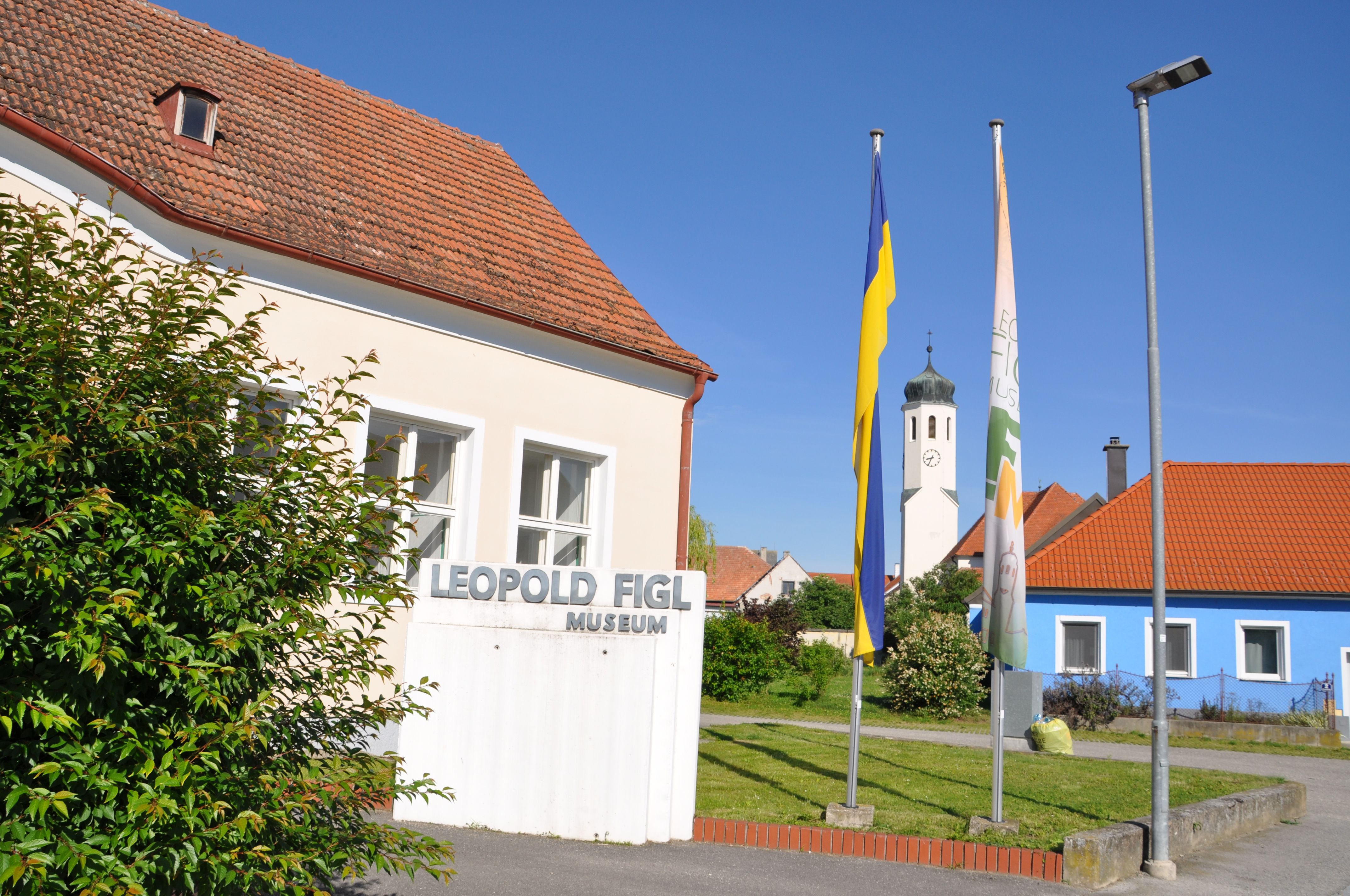 Leopold Figl Múzeum, a háttérben zászlókkal és a templom tornyával.