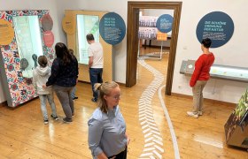 Az emberek egy m&uacute;zeumban interakt&iacute;v ki&aacute;ll&iacute;t&aacute;sokat n&eacute;znek meg sz&ouml;veges t&aacute;bl&aacute;kkal &eacute;s ki&aacute;ll&iacute;t&aacute;si t&aacute;rgyakkal.