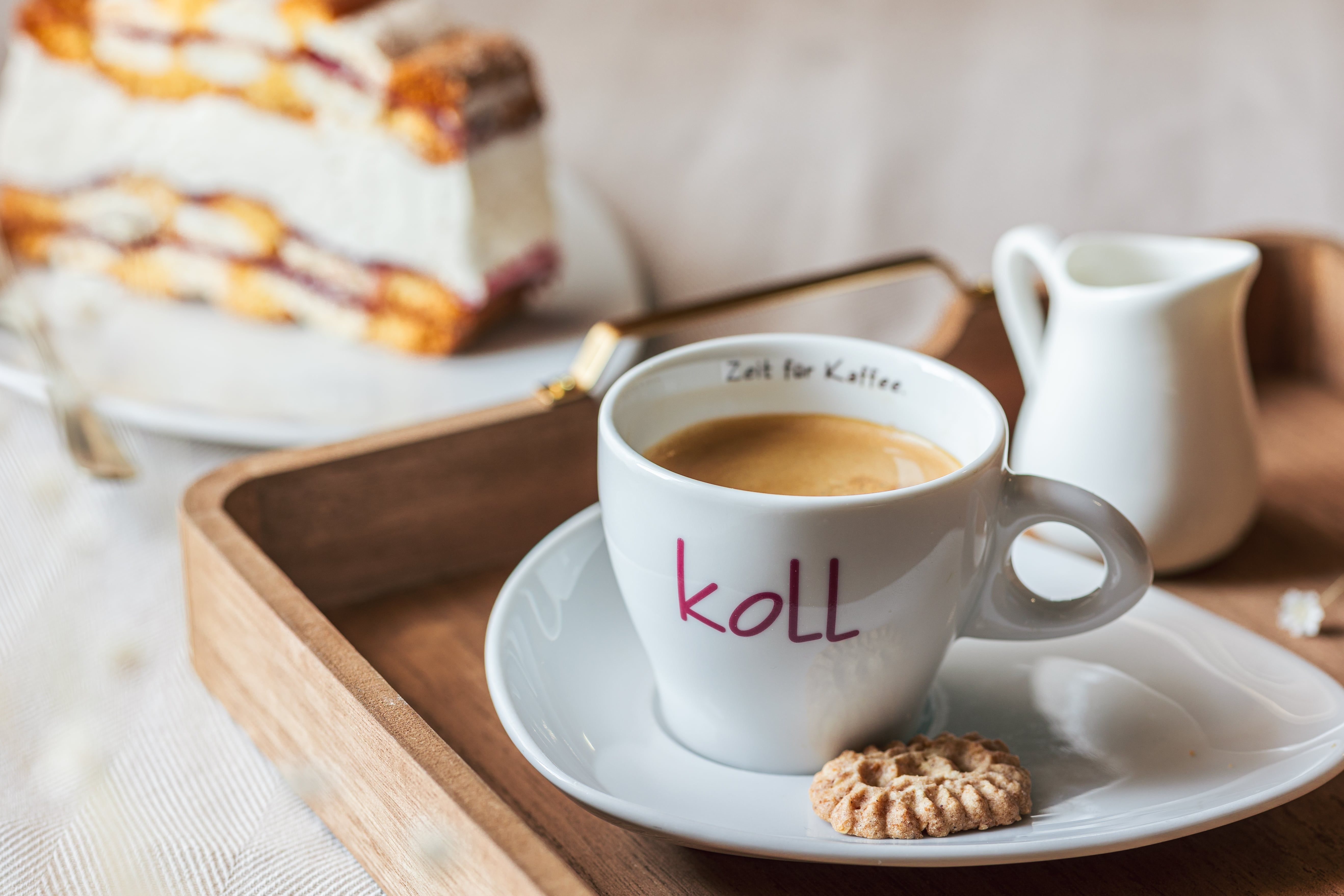 Egy csésze kávé keksszel egy tálcán, a háttérben egy szelet sütemény.