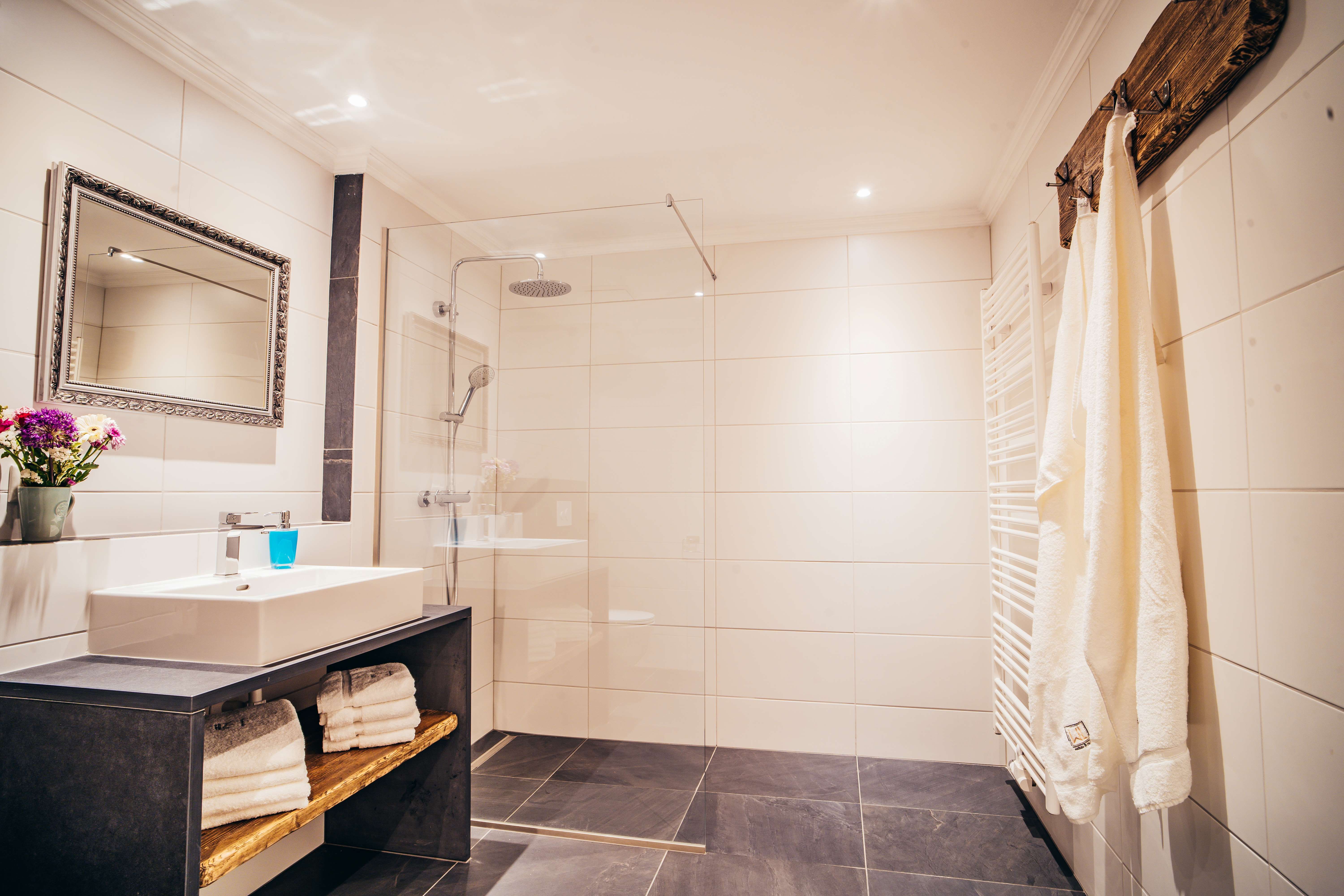 Modern fürdőszoba nagy zuhanyzóval, mosdókagylóval, tükörrel és törölközőkkel.