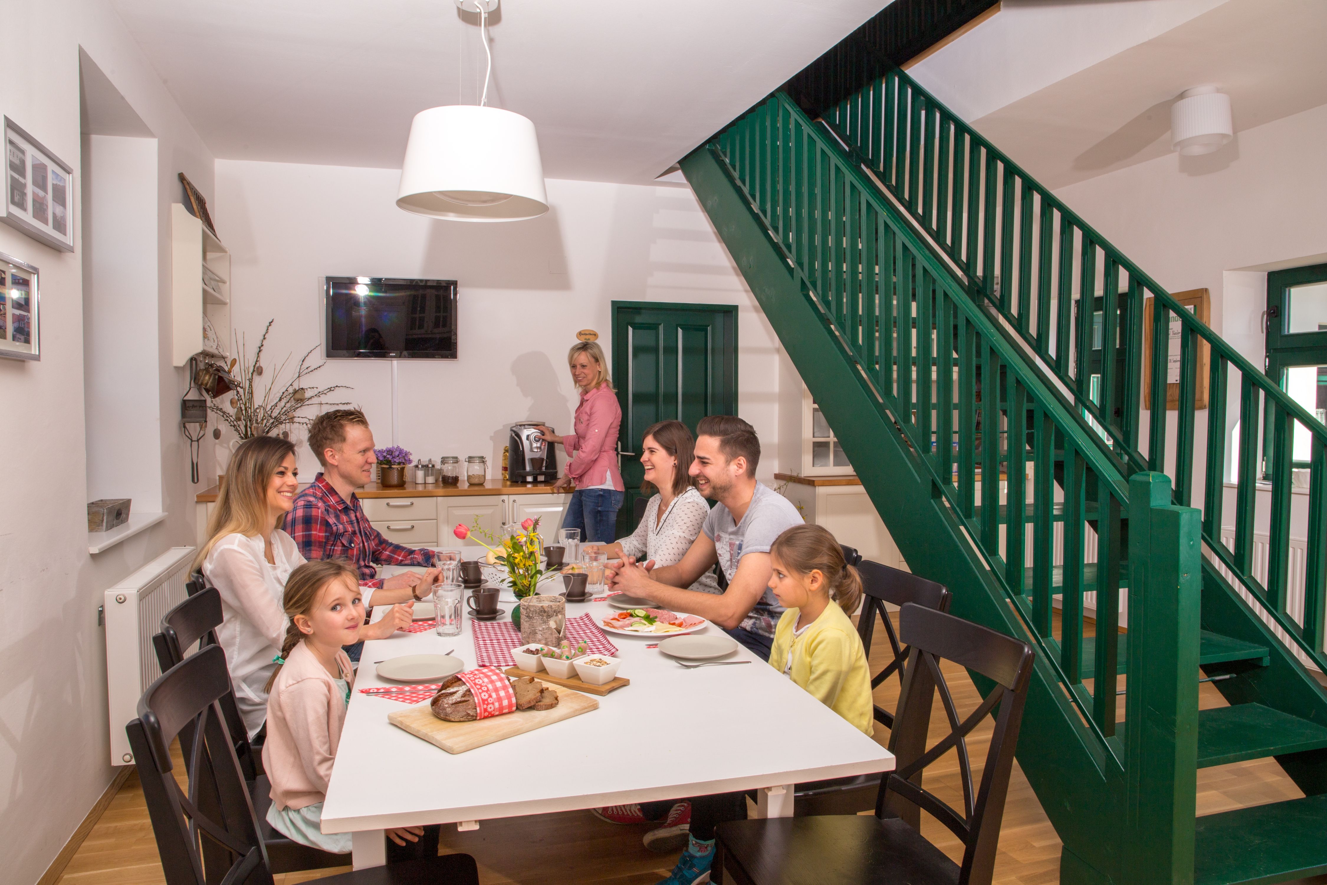 Család ül egy asztalnál egy modern étkezőben, zöld lépcsőházzal.