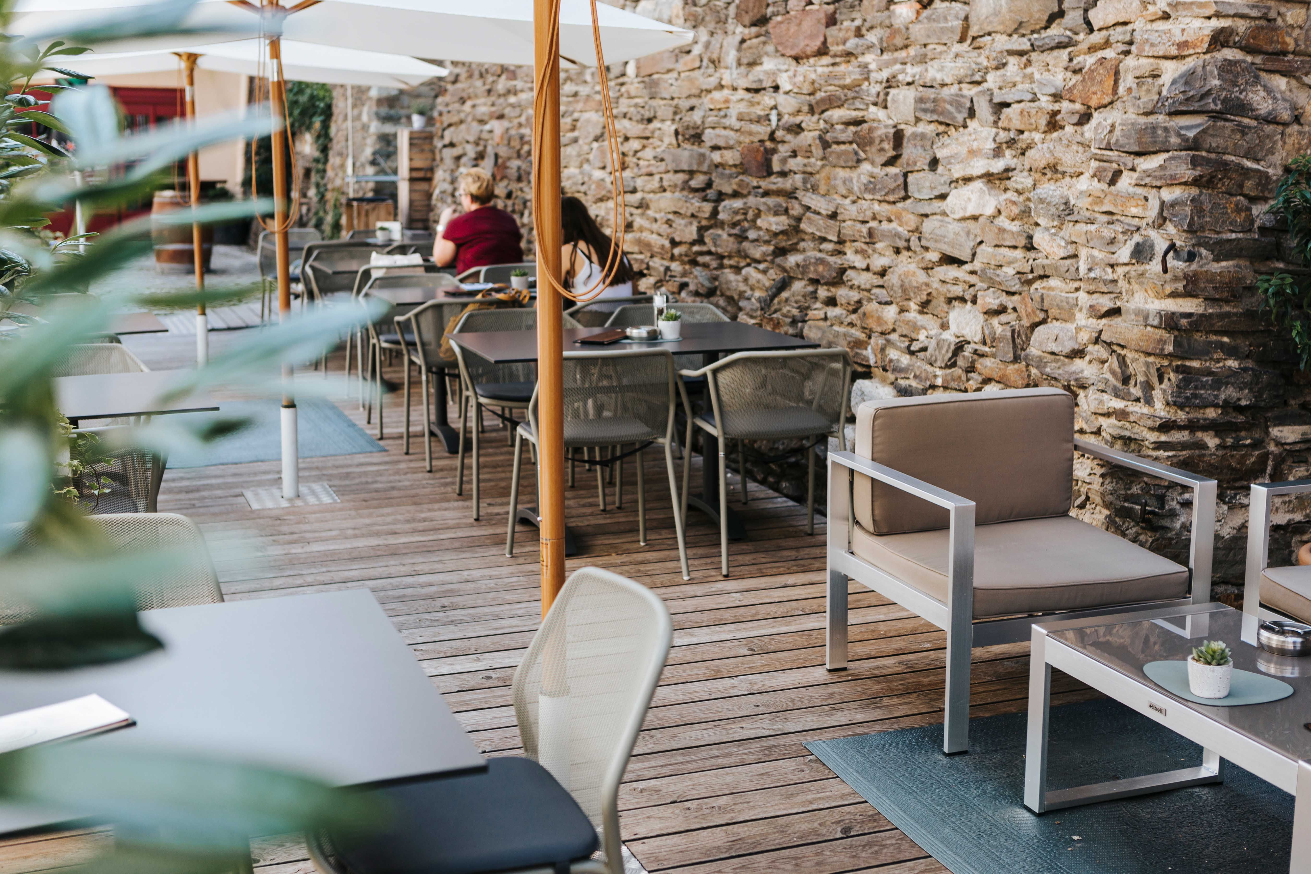 Egy kávézó hangulatos kültéri területe fapadlóval, modern bútorokkal és kőfallal.