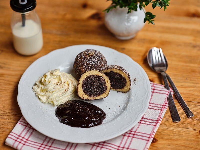 Tálalja a mákos gombócokat, a tejszínt és a csokoládémártást egy faasztalon.