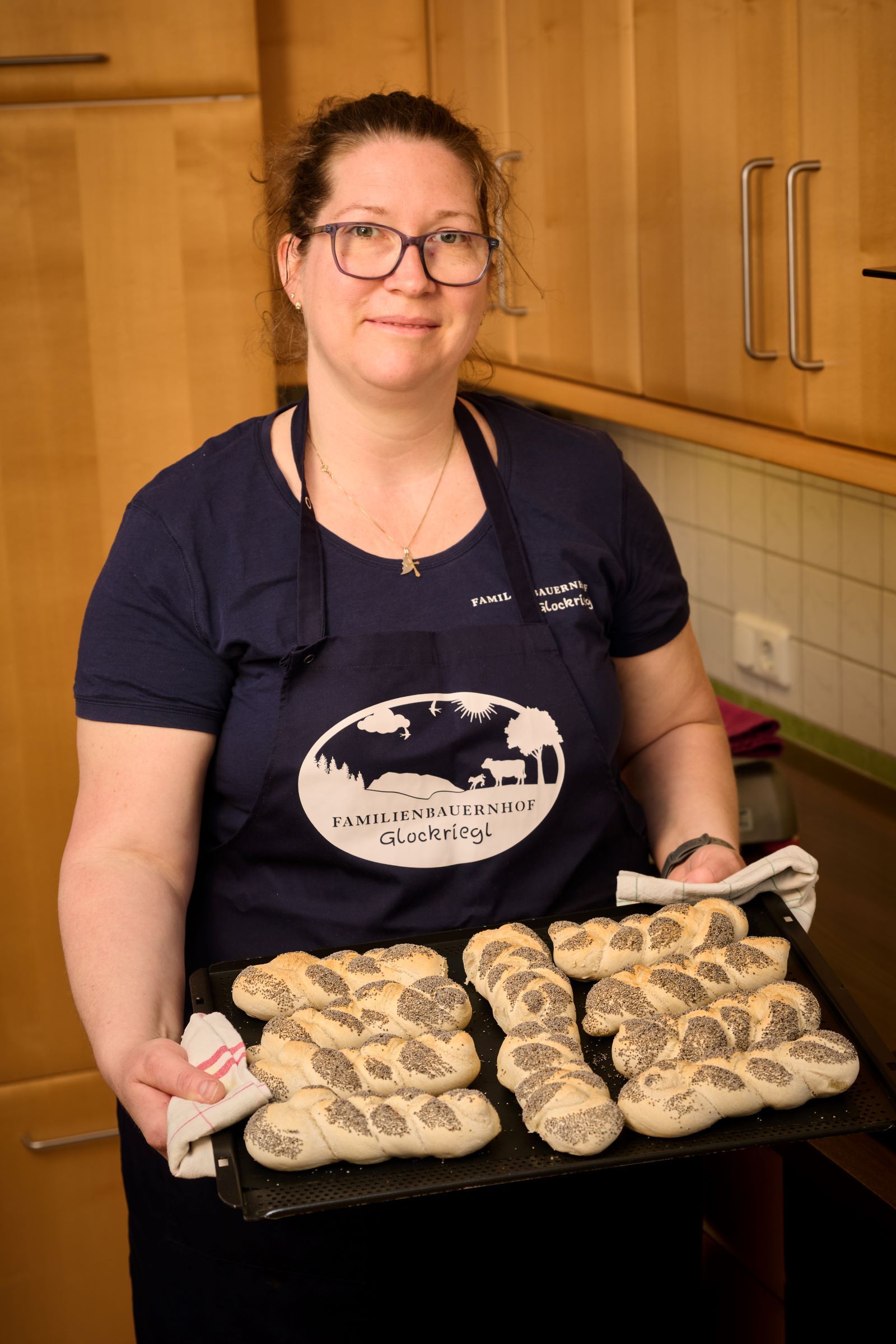 Egy nő a konyhában egy tálca frissen sült mákos zsemlét tart a kezében.