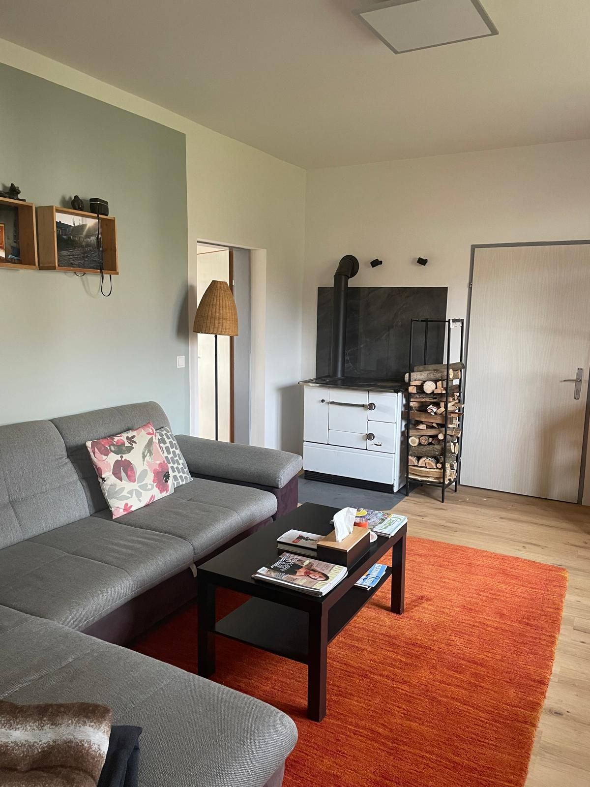 Hangulatos nappali szürke kanapéval, dohányzóasztallal, piros szőnyeggel és fatüzelésű kályhával.