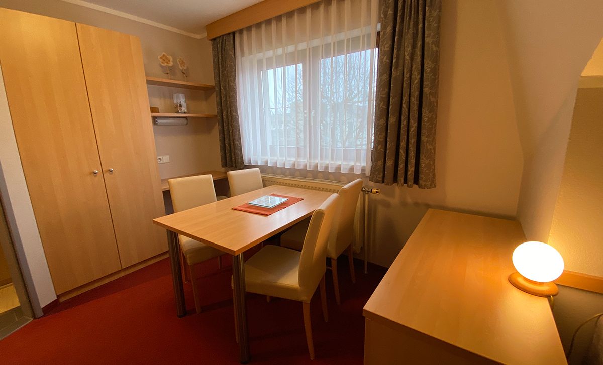 Hangulatos szoba fabútorokkal, asztallal, székekkel és függönyös ablakkal.