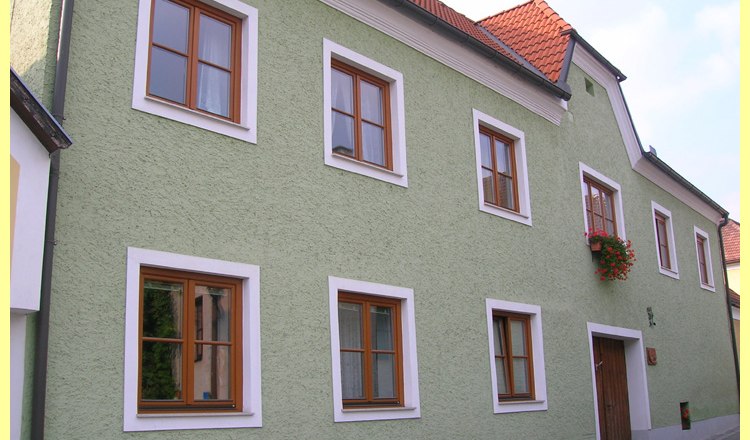 Z&ouml;ld h&aacute;z piros tetőcser&eacute;ppel &eacute;s fa ablakokkal.