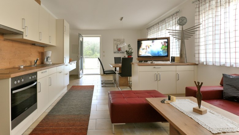 Modern &eacute;tkezős konyha felszerelt konyh&aacute;val, &eacute;tkezőasztallal, TV-vel &eacute;s piros &uuml;lőb&uacute;torral.