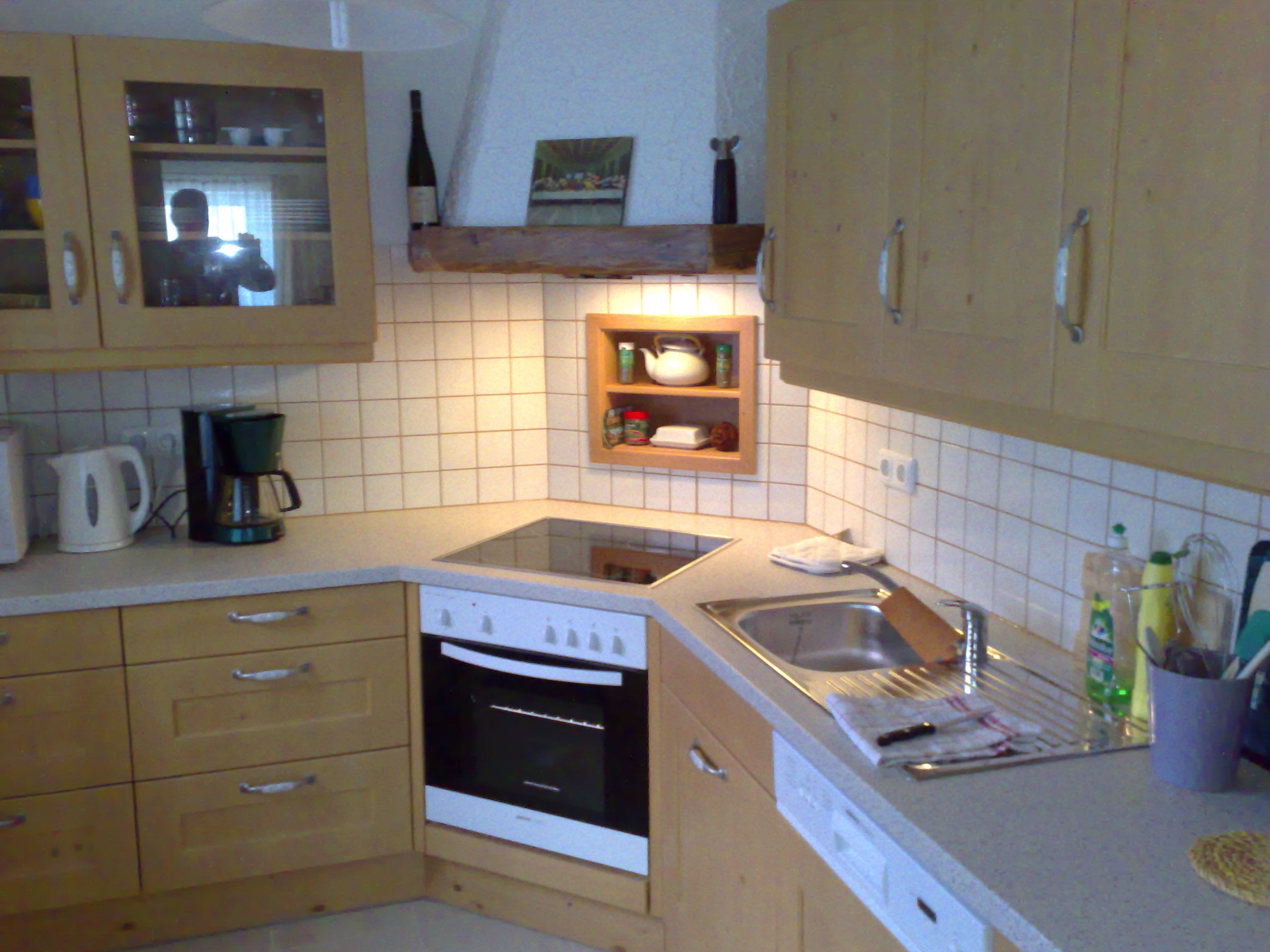 Konyha fából készült szekrényekkel, tűzhely, mosogató és kávéfőző.