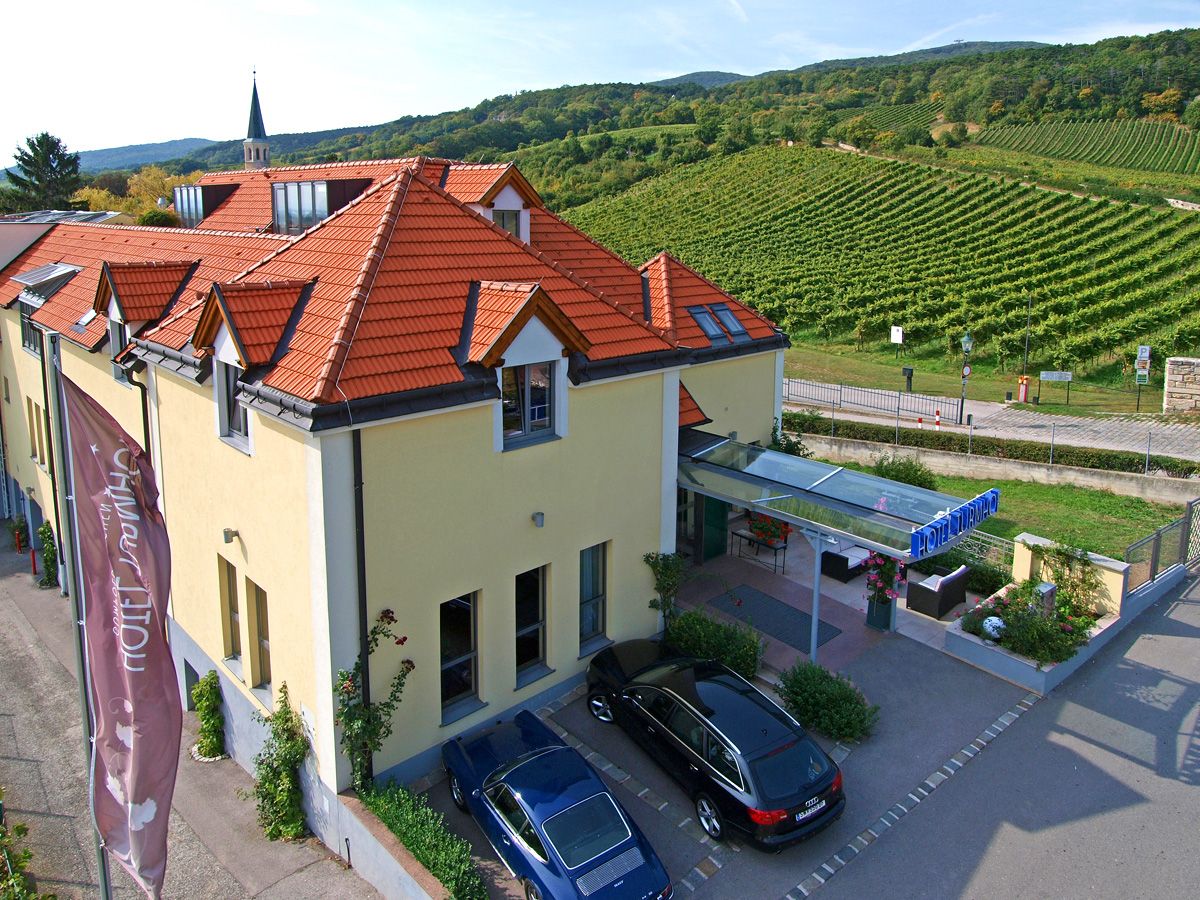 A Hotel Turmhof külső nézete a vörös tetőkkel és a környező szőlőültetvényekkel.
