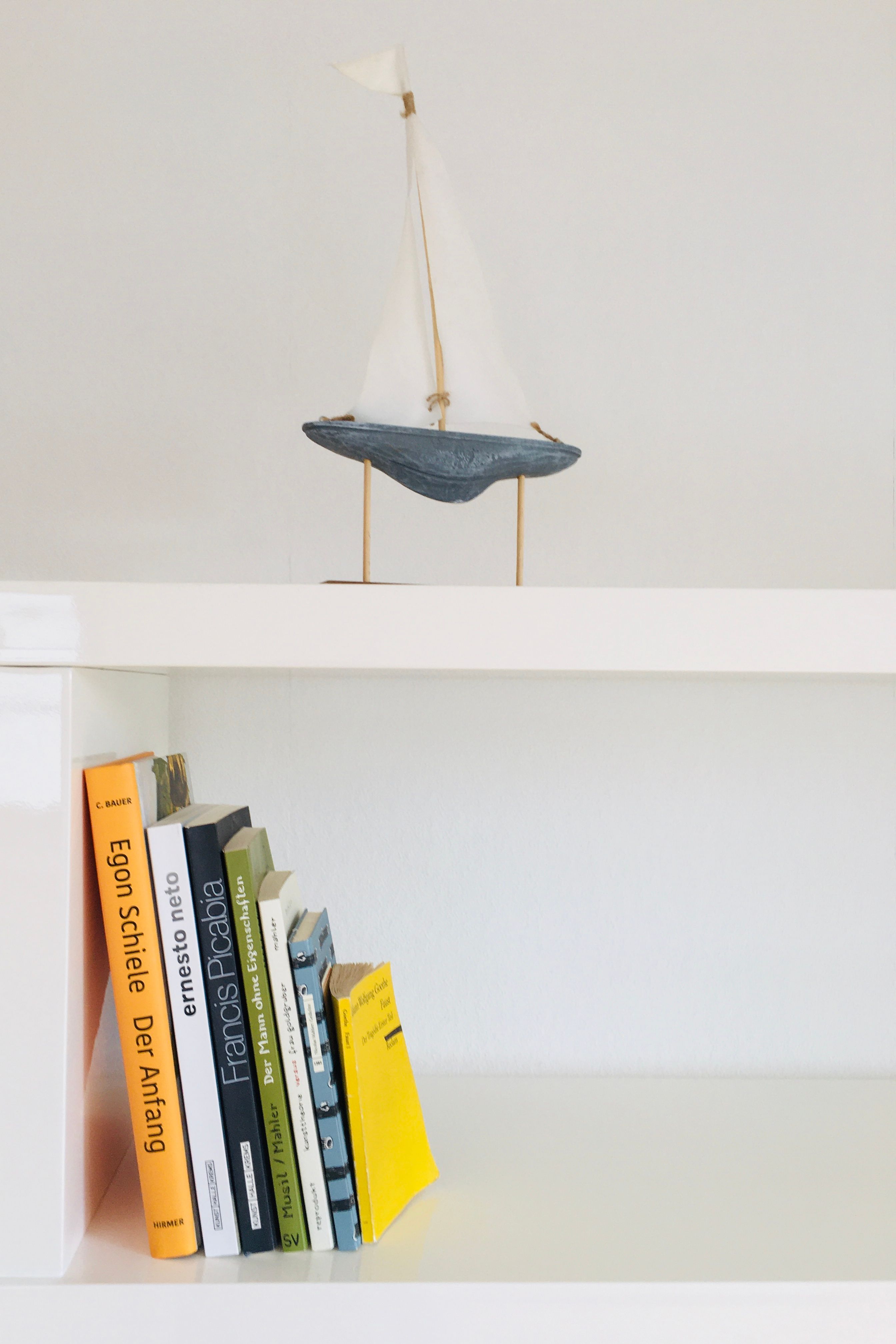Egy fehér polc könyvekkel és egy kis vitorlással díszítve.