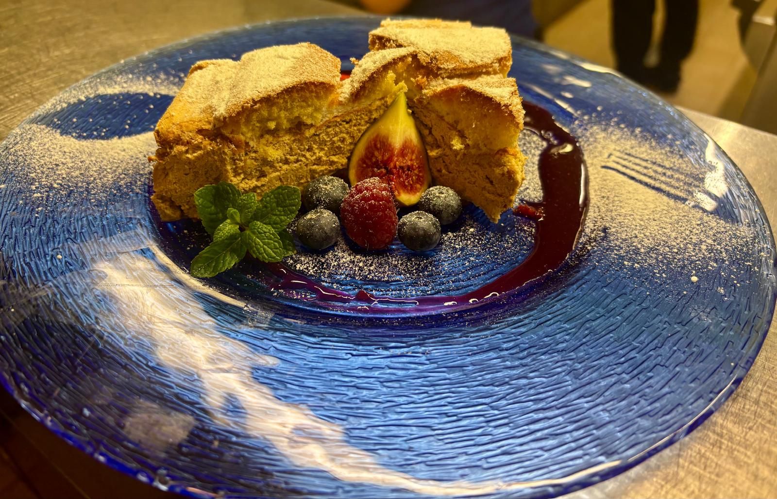 Desszert kék tányéron, bogyókkal, fügével és mentalevelekkel díszítve, porcukorral meghintve.