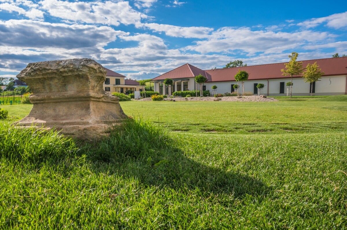 Borászat pázsittal és antik kővel az előtérben.