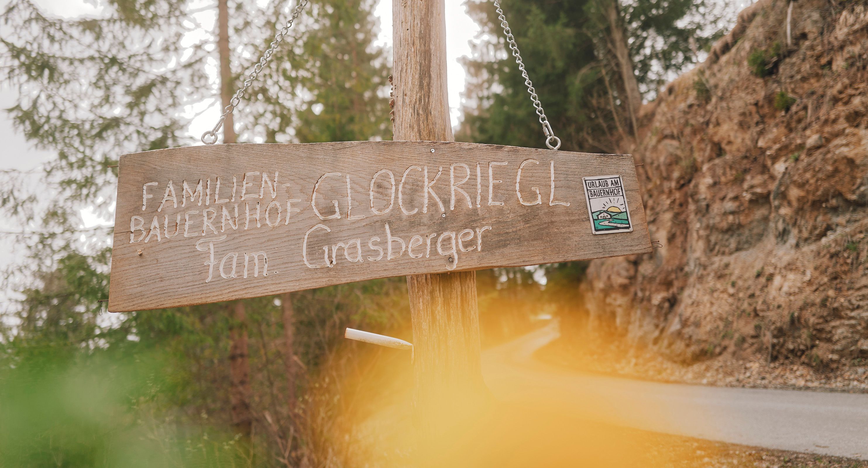"Familienbauernhof Glockriegl Fam. Grasberger" feliratú fatábla egy erdei ösvényen.