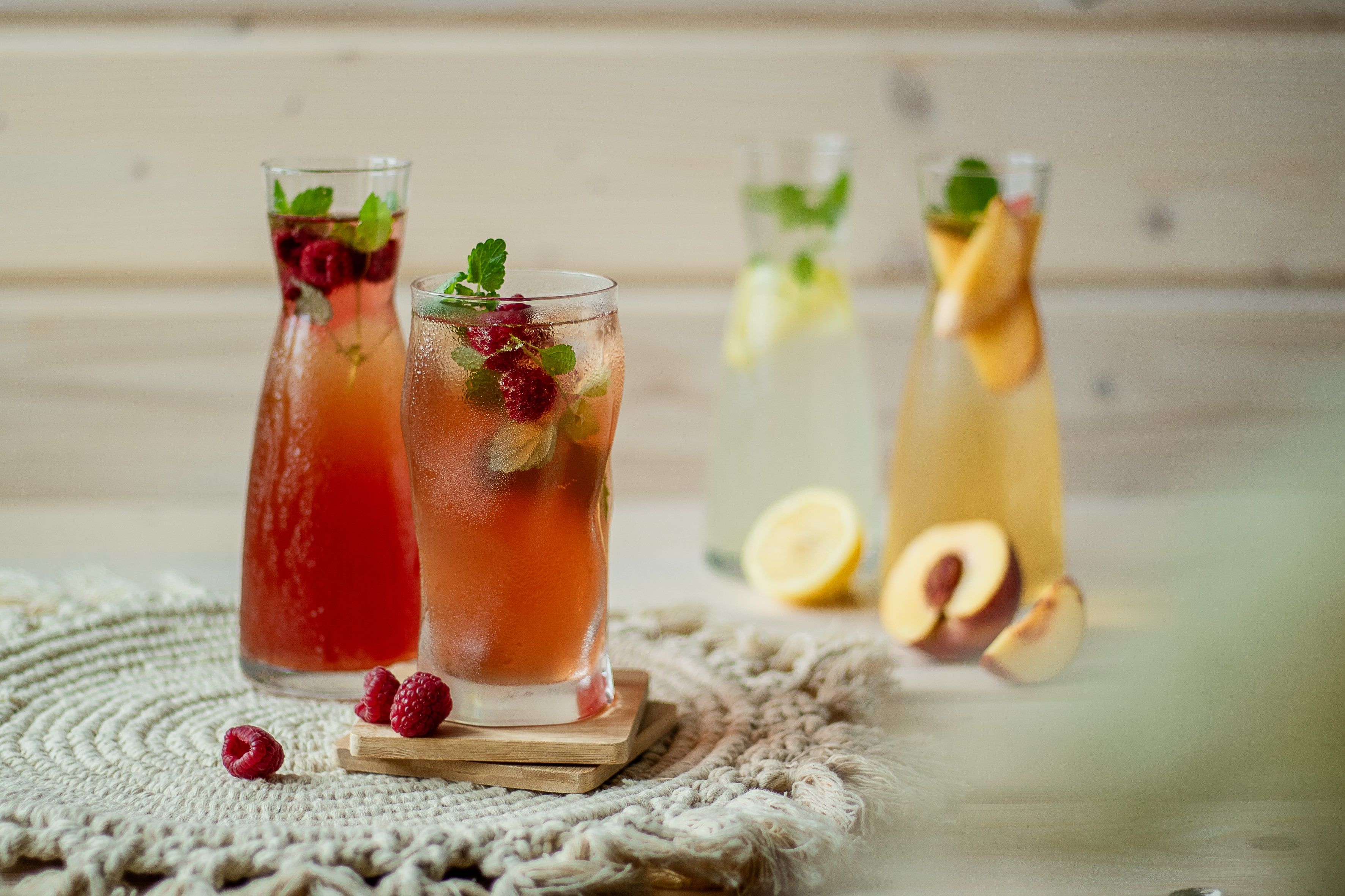Különböző poharak limonádéval, gyümölcsökkel és mentával díszítve egy asztalon.