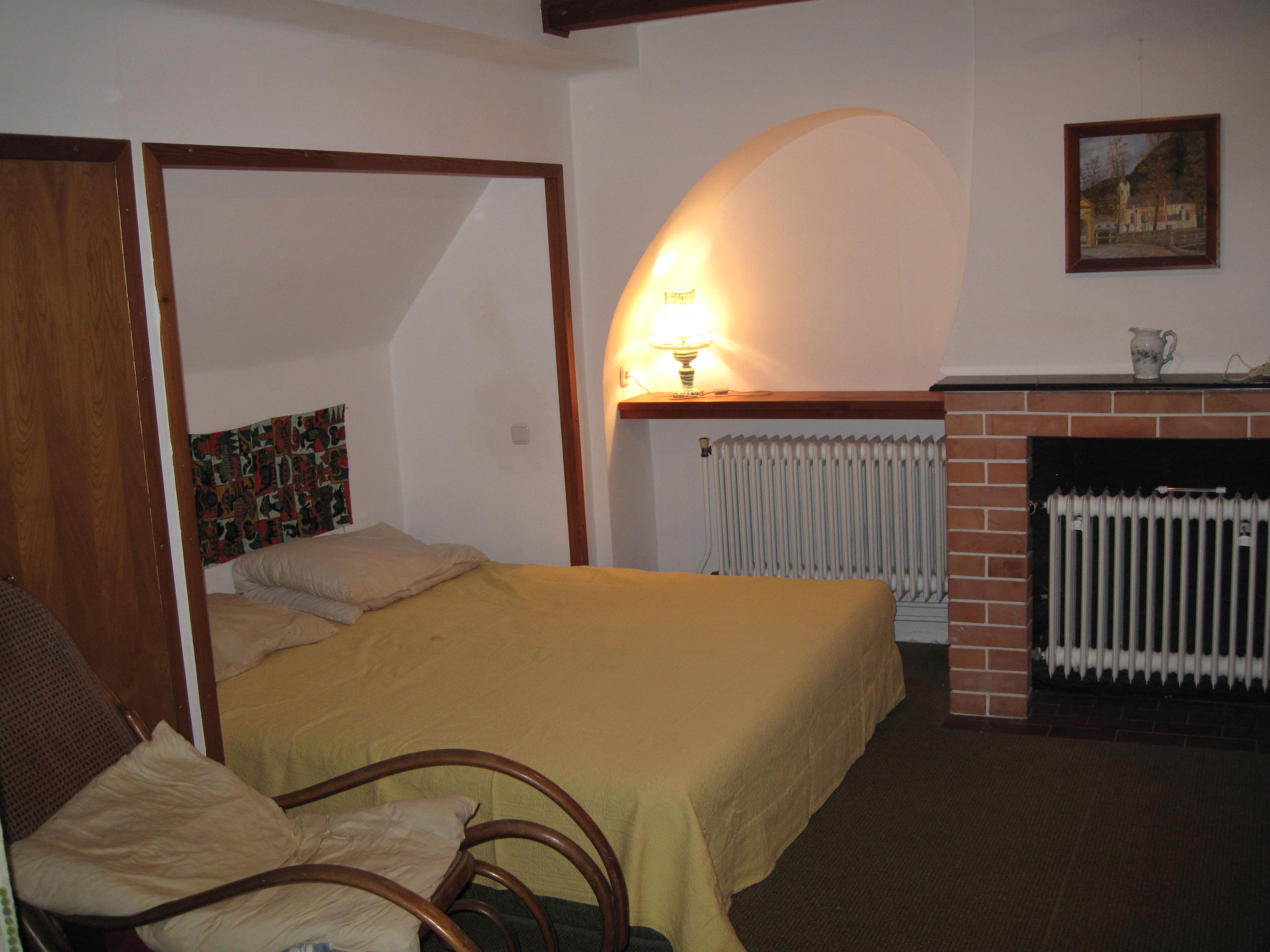 Hangulatos hálószoba egy ággyal, egy karosszékkel, egy lámpával és egy kandallóval.