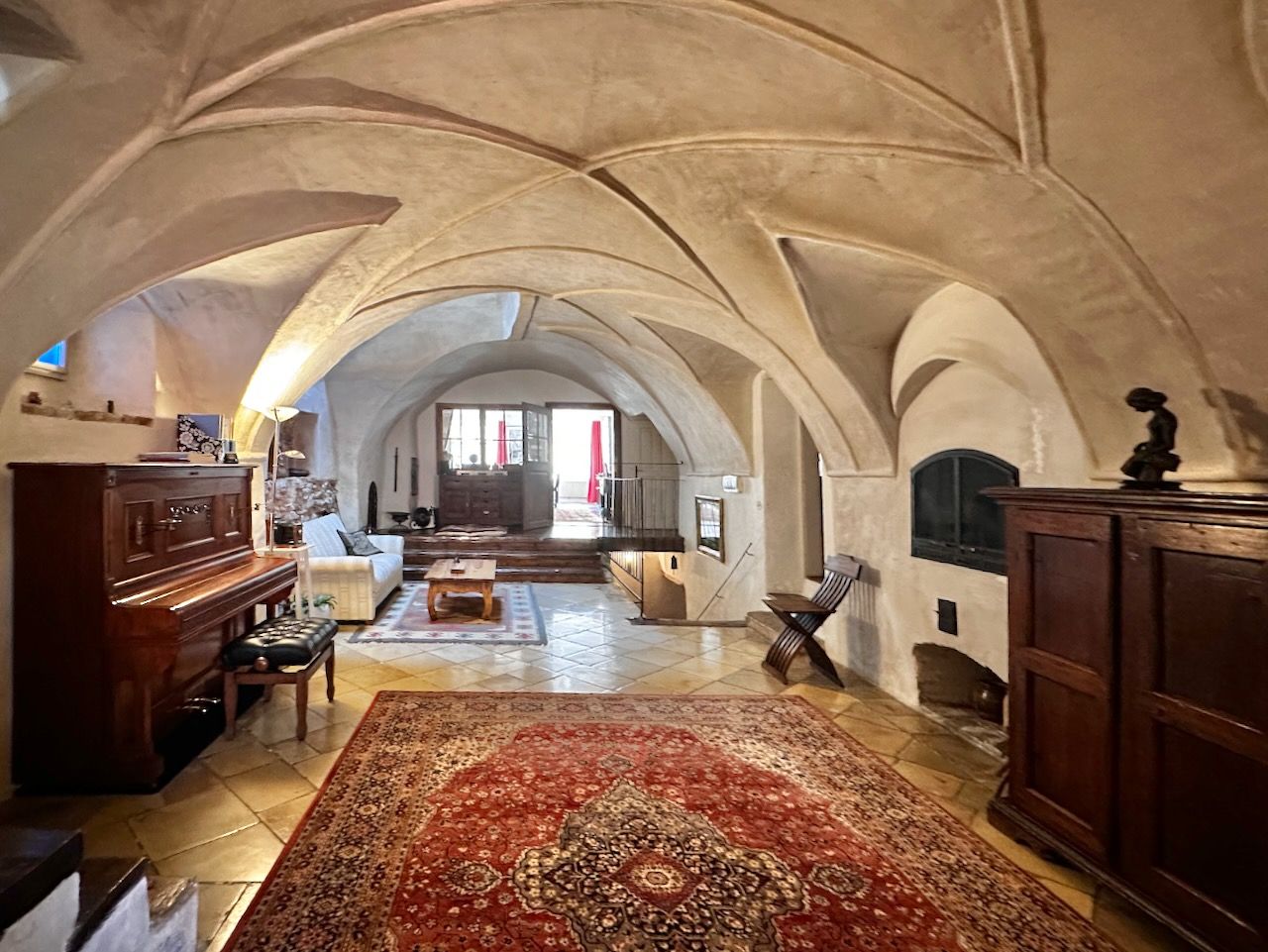 Történelmi fogadóterem boltíves mennyezettel, szőnyeggel, zongorával és fabútorokkal.