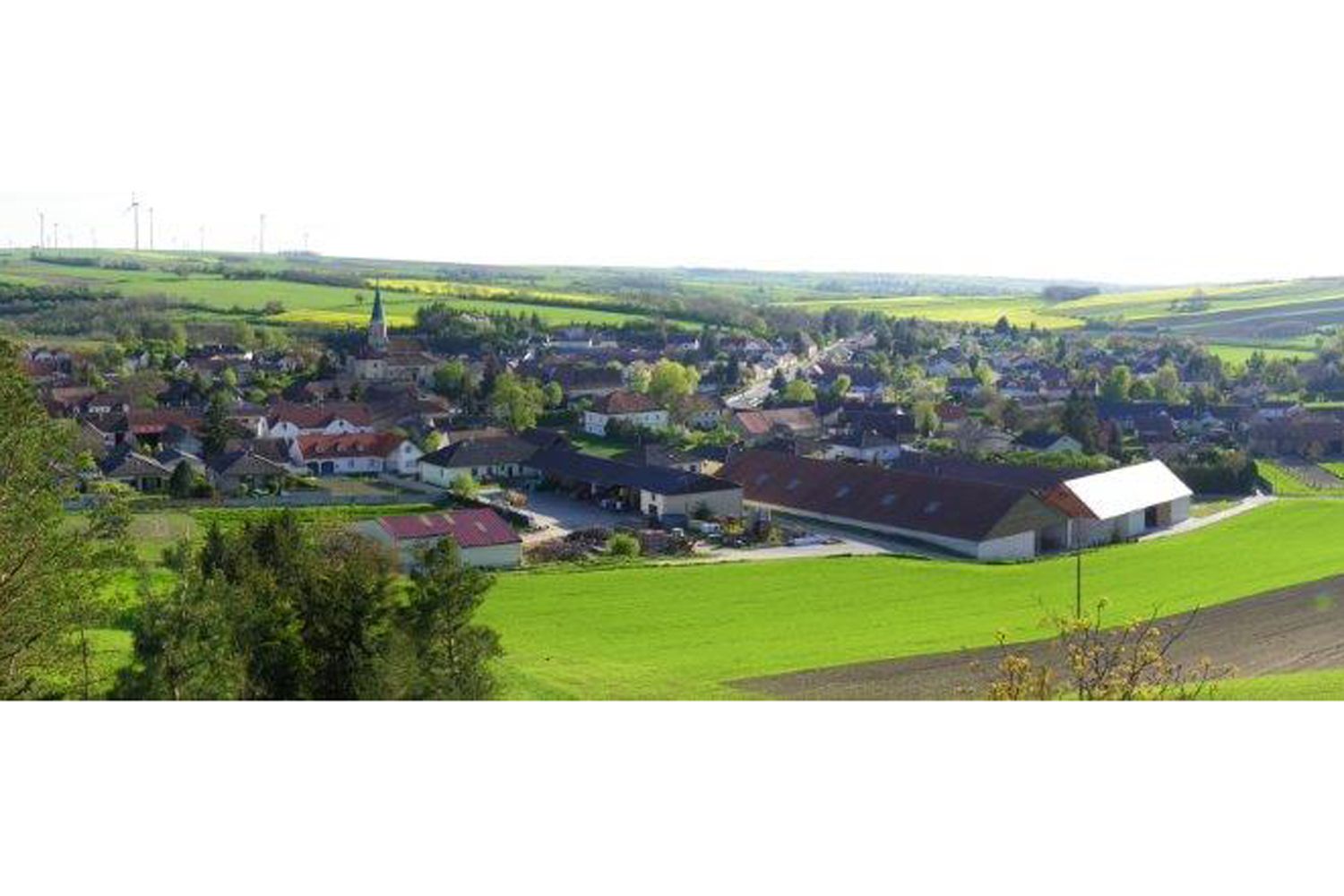 Tájkép faluval és templommal, mezőkkel körülvéve.
