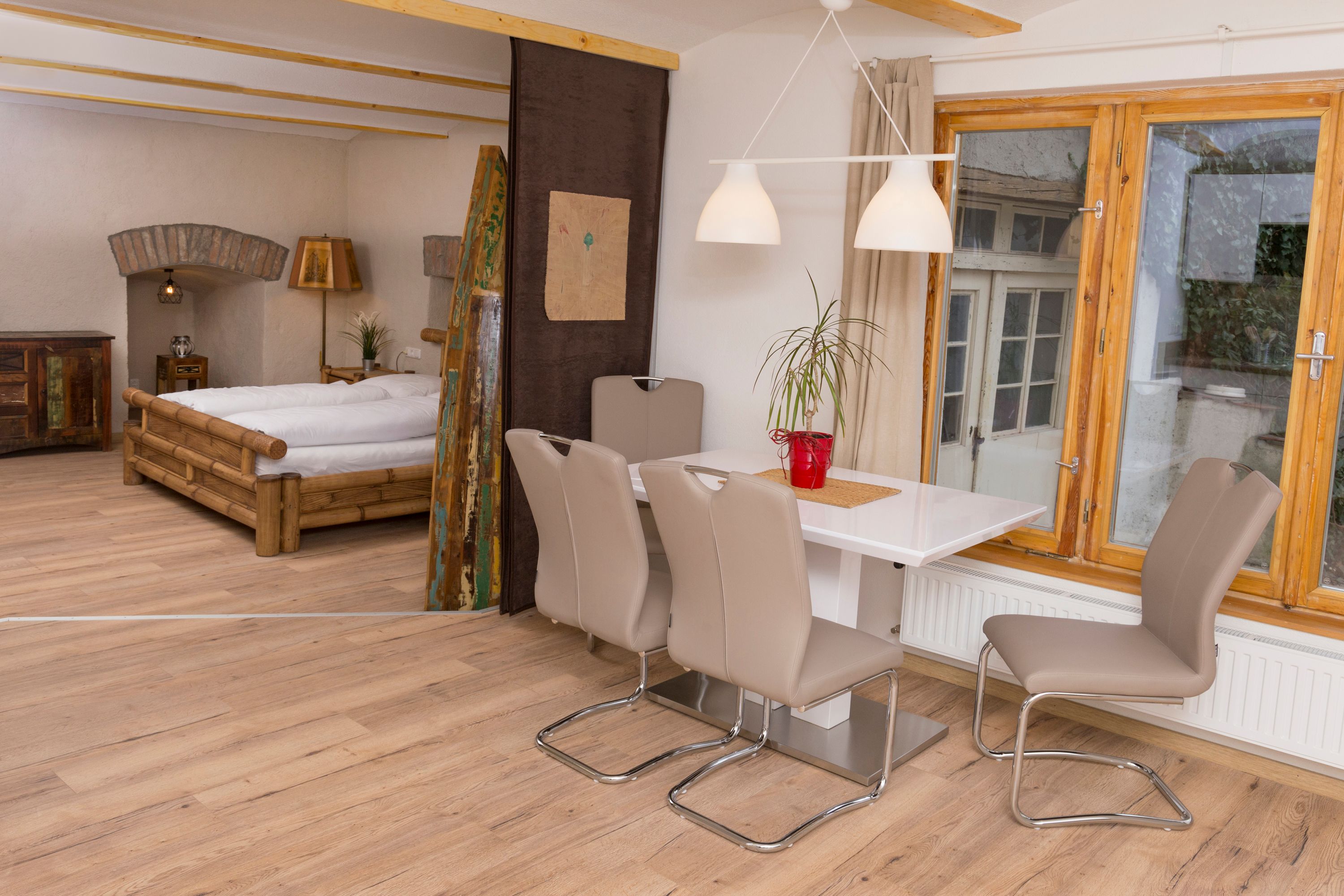 Egy nyaraló belső nézete étkezőasztallal, székekkel, ággyal és ablakkal.