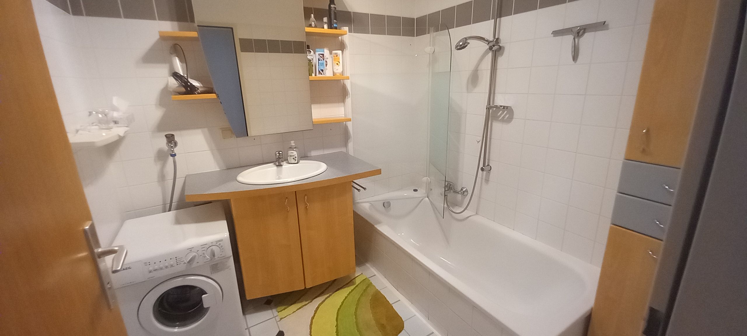 Modern fürdőszoba mosógéppel, mosdókagylóval, káddal és polcokkal.