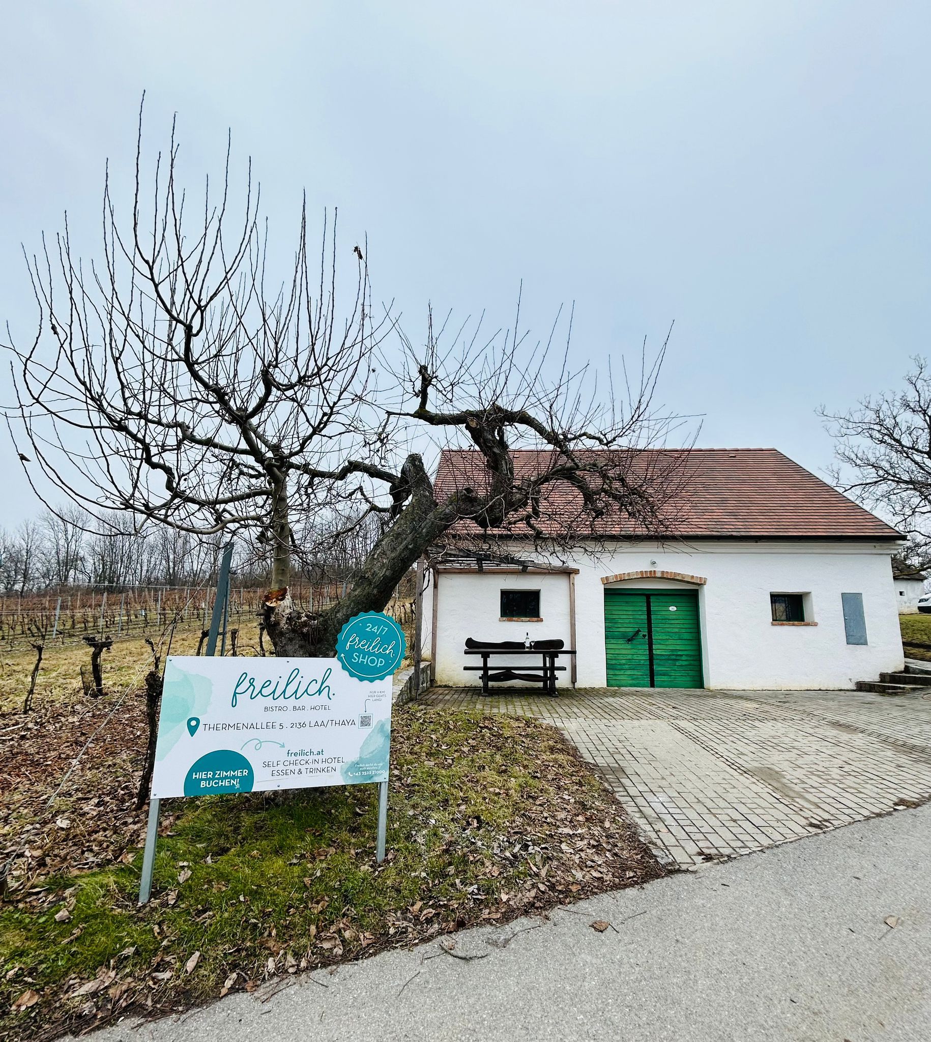 Fehér épület zöld kapuval és "freilich" felirattal vidéki környezetben.