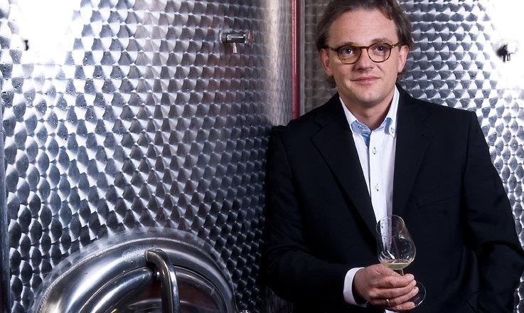 Egy &ouml;lt&ouml;ny&ouml;s f&eacute;rfi borospoharat tart egy nagy rozsdamentes ac&eacute;ltart&aacute;ly előtt.